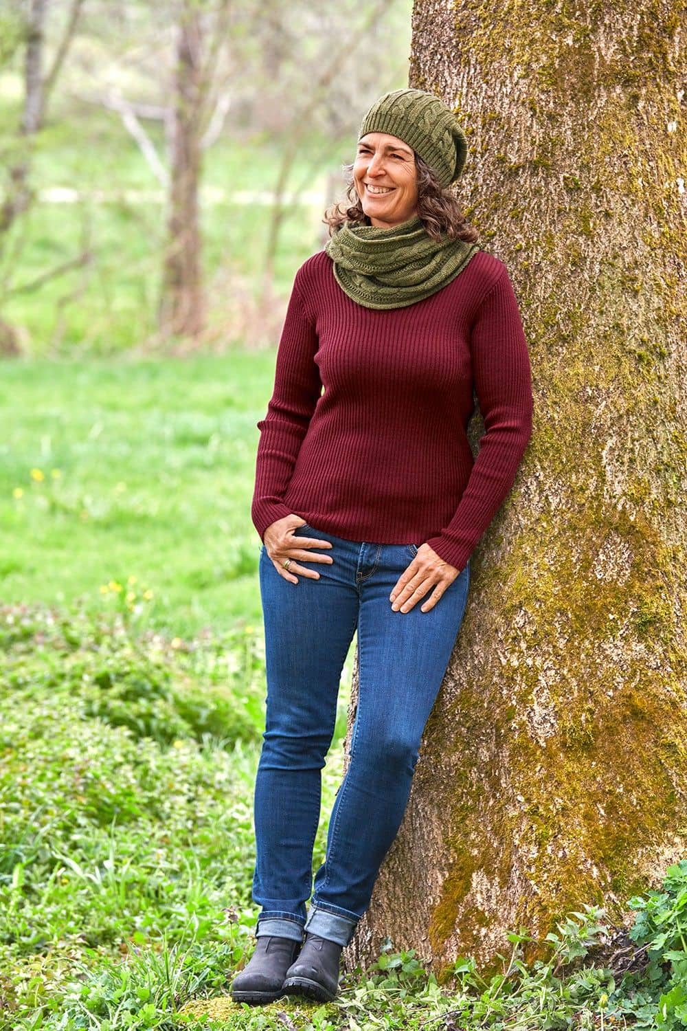 Frau mit rotem Shirt, Jeans, Mütze und grünem Loopschal aus bio Wolle (kbT) vom Finkhof mit Zopfmuster