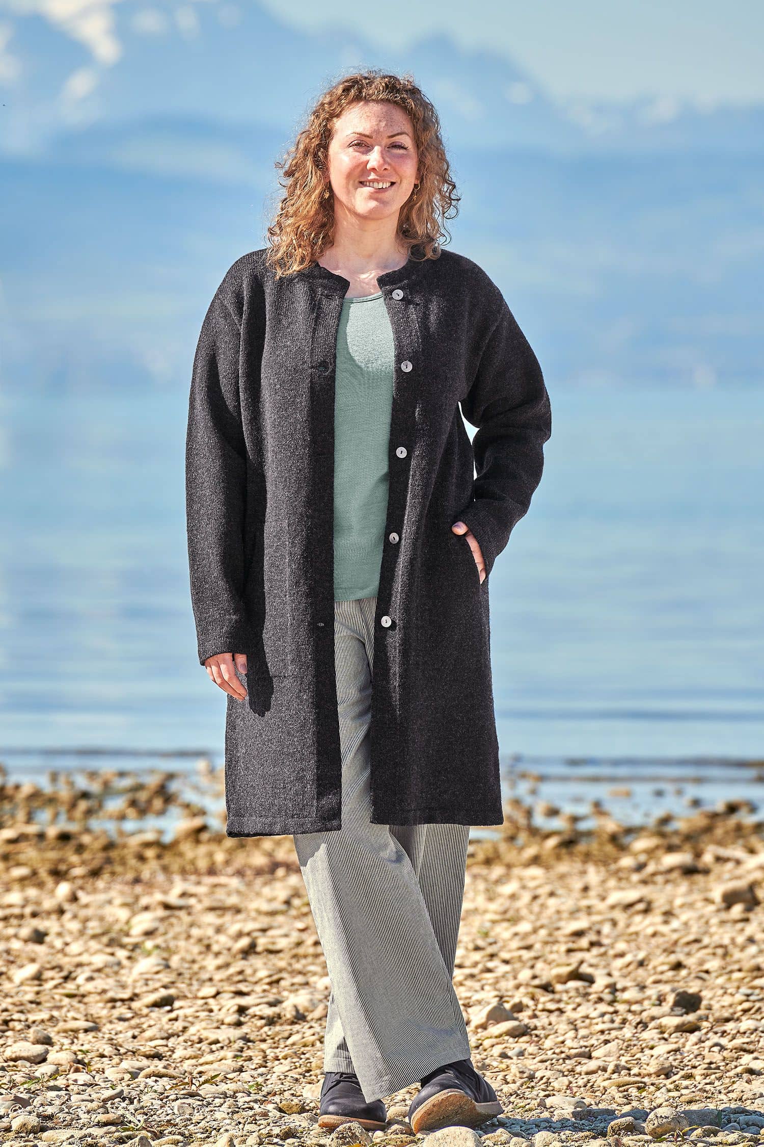 Finkhof-Strickmantel anthrazit Gr. XL Frau trägt anthrazitgrauen Strickmantel aus bio Wolle (kbt) vom Finkhof, ein blaues Shirt und eine Stoffhose
