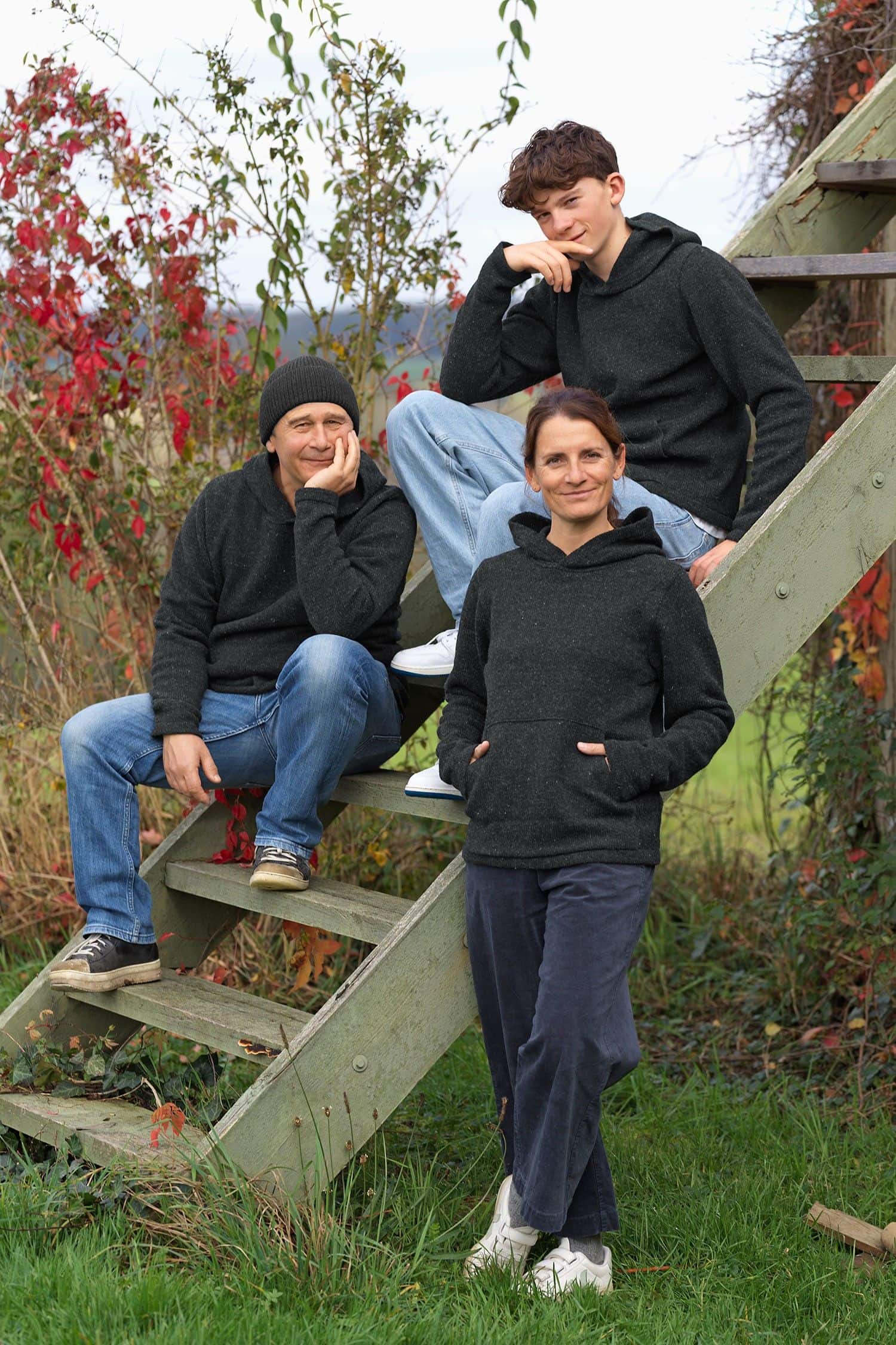 Personen sitzen auf Treppe und tragen dunkelgrauen Kapuzenpullover vom Finkhof aus bio Wolle (kbT)