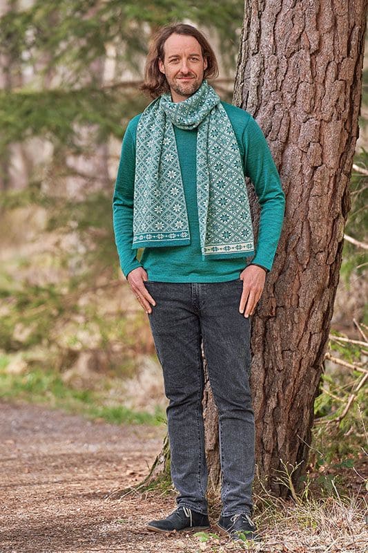 Mann steht vor Baum und trägt petrolblaues Wollshirt aus bio Wolle (kbT) vom Finkhof mit türkis gemustertem Schal