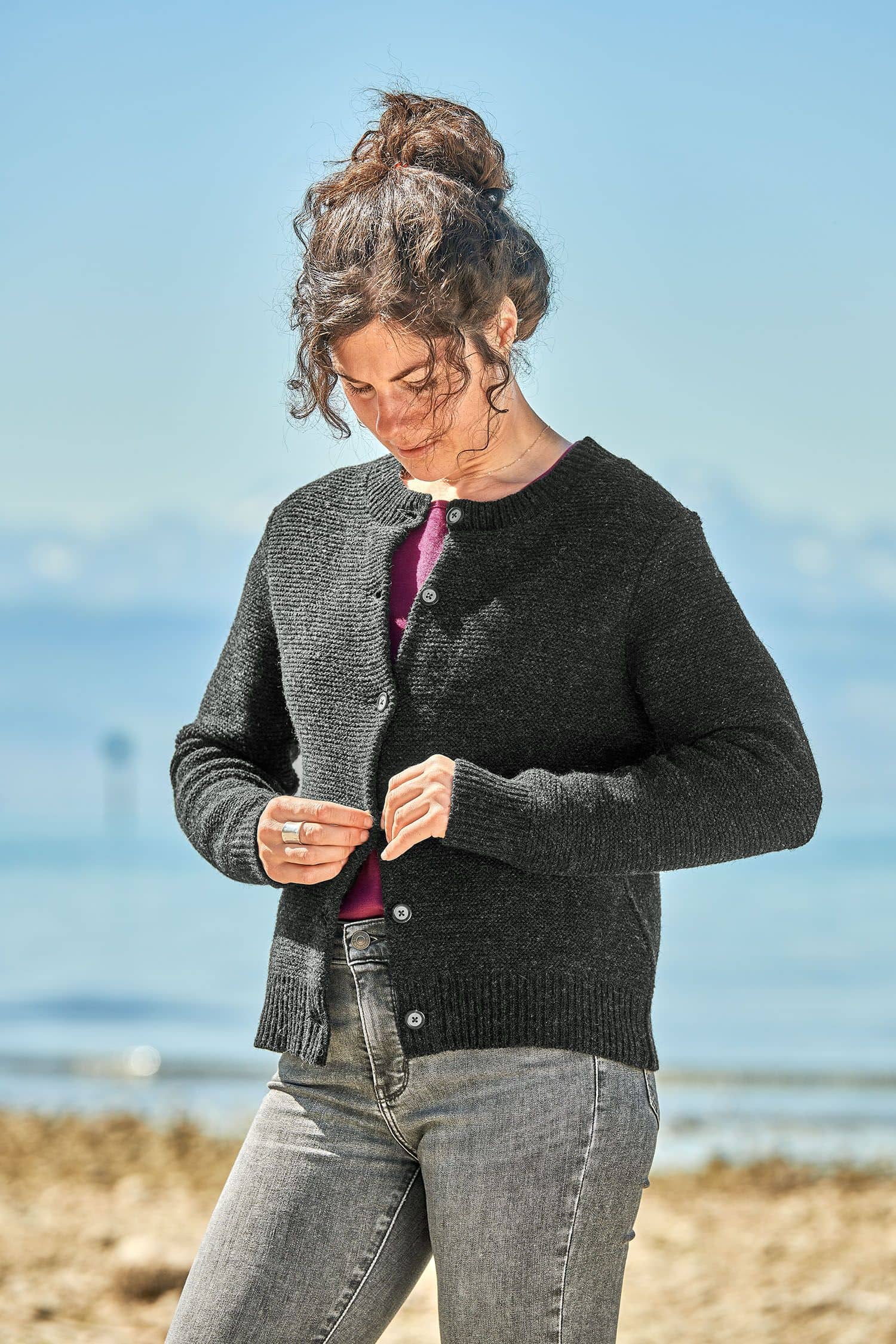 Frau trägt eine graue Jeans, ein lila Shirt und eine dunkelgraue Strickjacke vom Finkhof aus bio Merinowolle (kbT)