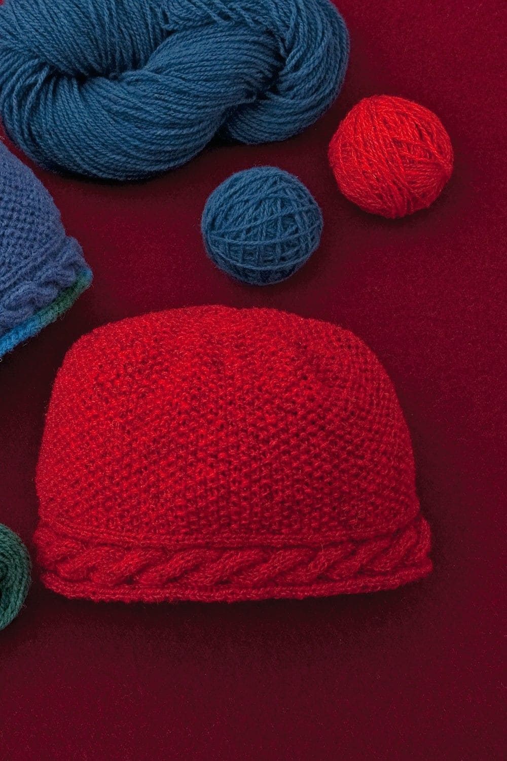 Strickmütze aus dünner roter Finkhof Merinowolle aus bio Wolle (kbT) auf rotem Untergrund mit blauer Wolle daneben