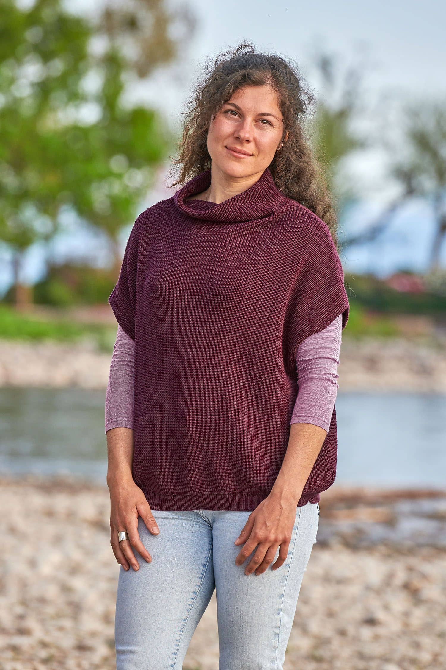 Frau trägt einen burgunderroten Strickpullunder aus bio Wolle (kbT) vom Finkhof mit einem lila Shirt und Jeans