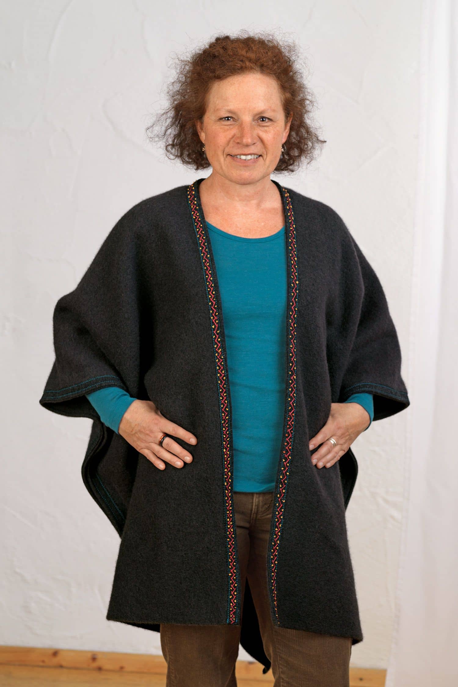 Frau mit türkisem Shirt trägt Poncho mit gestickten Details