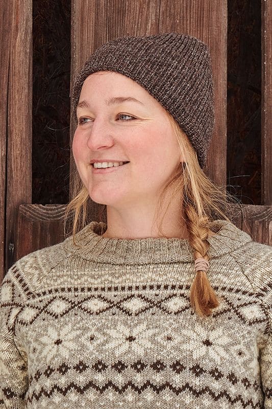 Frau trägt eine braune Finkhof Mütze aus bio Wolle (kbT) und einen Norwegerpulli vom Finkhof