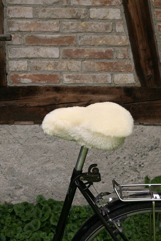 Fahrradsattelbezug relugan-gegerbt breit relugan gegerbter breiter Finkhof Sattelbezug aus bio Wolle (kbT) und Schaffell auf Fahrrad mit Steinwand im Hintergrund