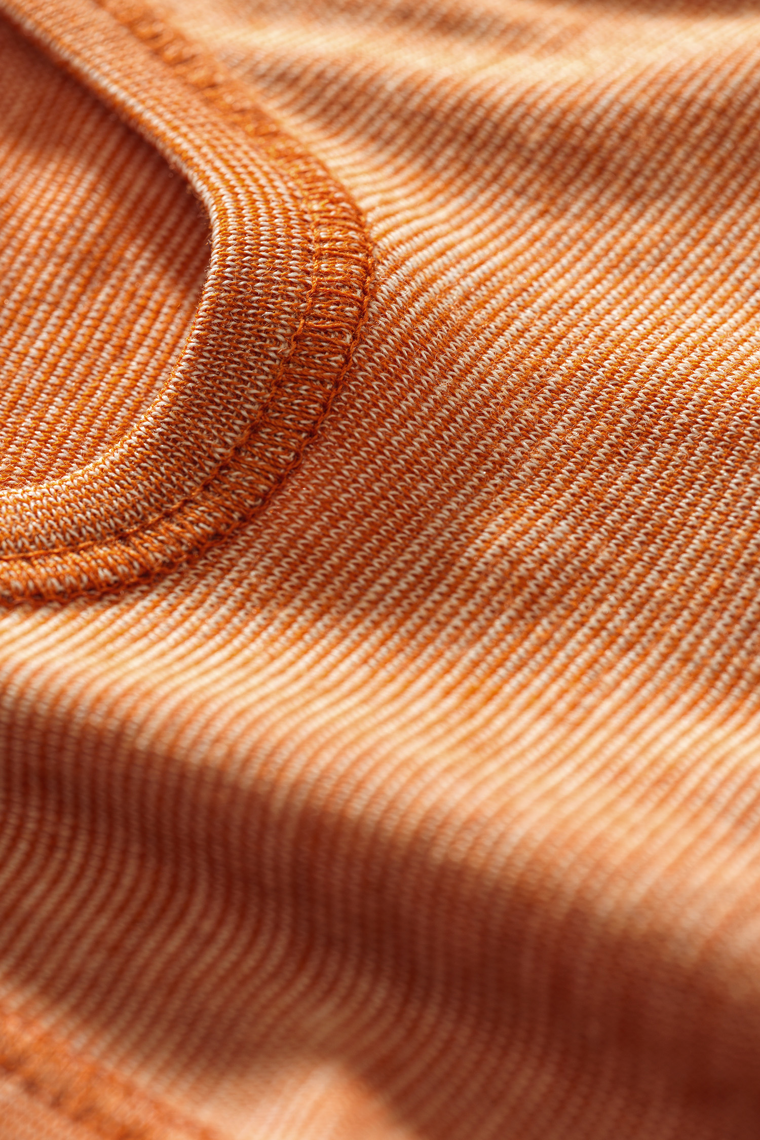 Nahaufnahme der Struktur des orangemelierten Babybodys aus Bio-Baumwolle, Bio-Merinowolle und Seide
