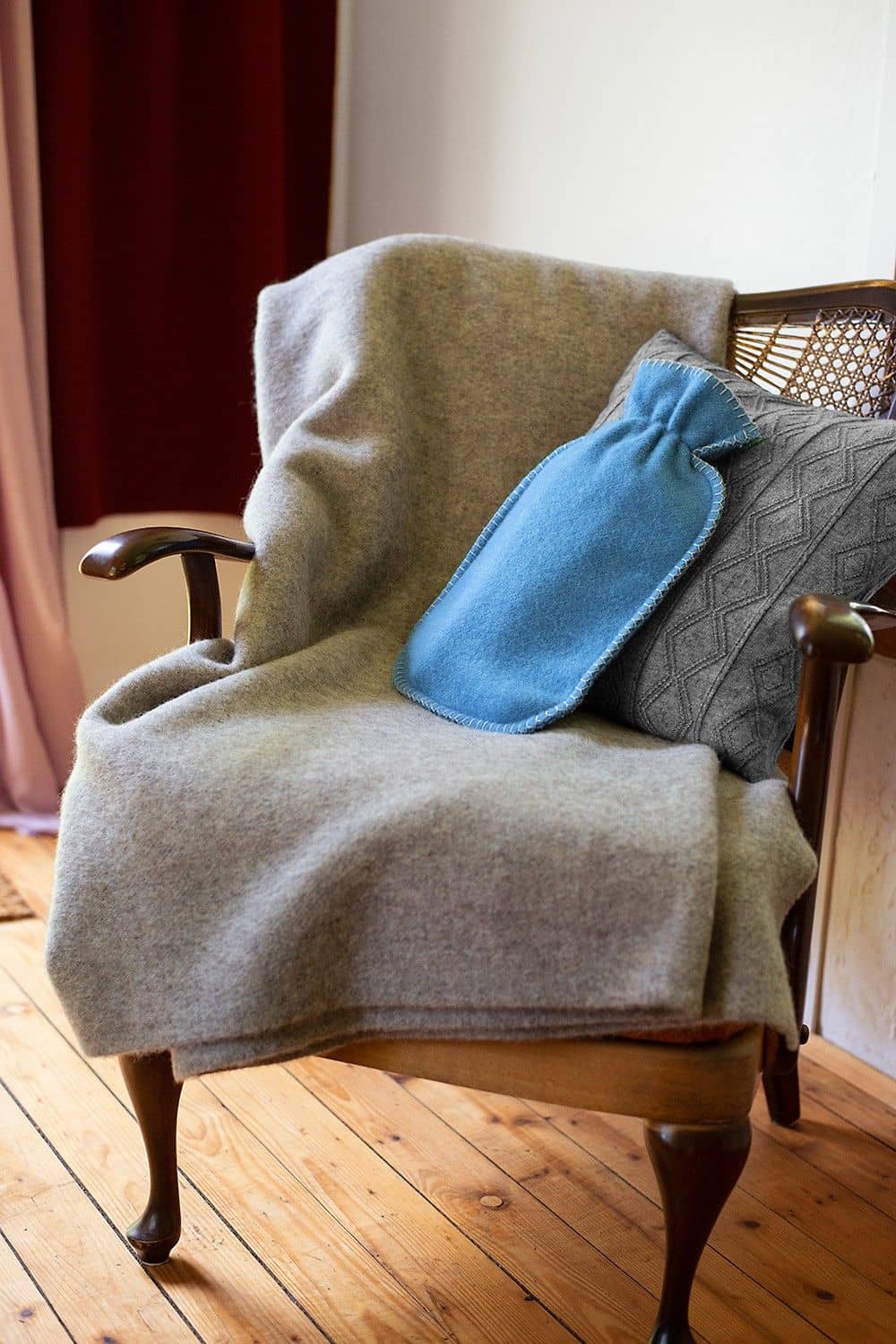 hellblauer Wärmflaschenbezug aus bio Wolle (kbT) vom Finkhof mit grauem Kissen und Teppich auf einem Sessel