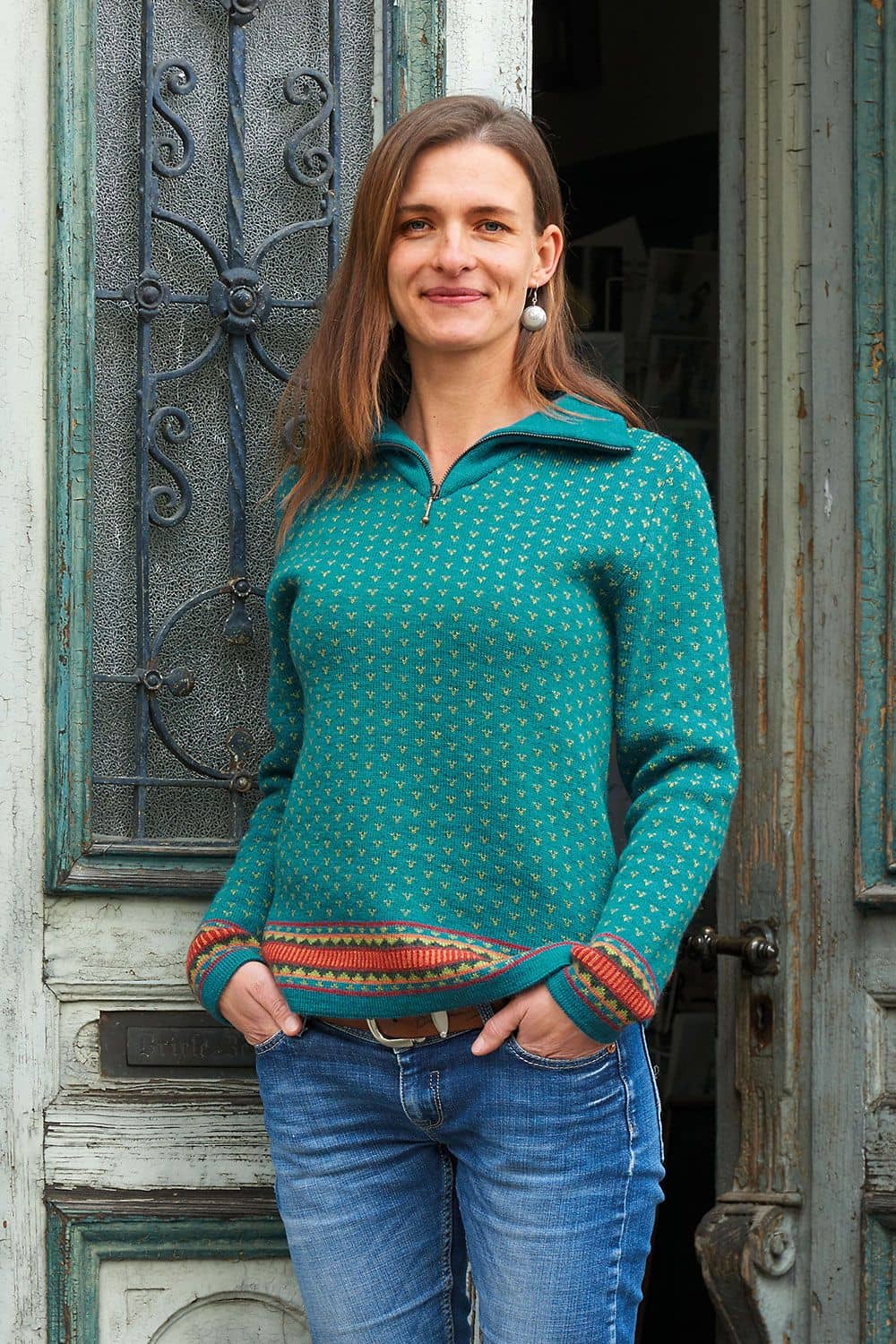 Norweger-Troyer Damen türkis Gr. M Frau steht vor Holztür und trägt türkisen Norweger Troyer aus bio Wolle (kbT)