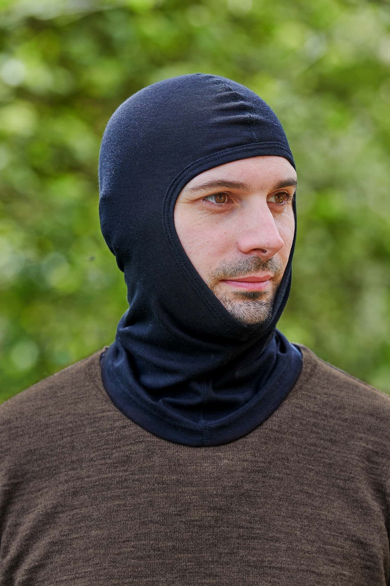 Mann mit braunem Pullover trägt eine schwarze Sturmhaube aus Bio-Schurwolle und Seide