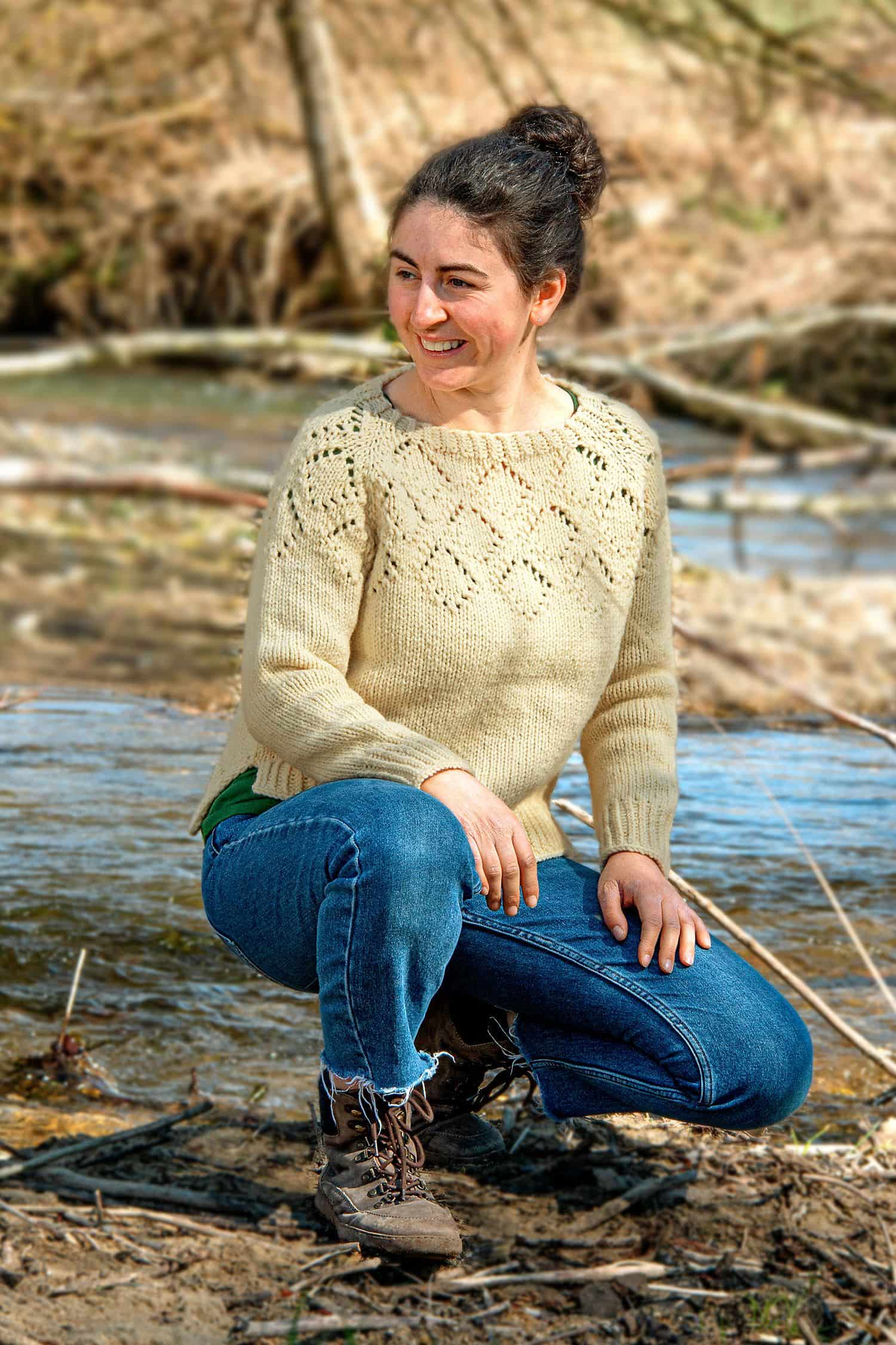 Frau kniet an Bach und trägt weißen Strickpulli als Beispiel für das Buch ,,Schnell gestrickt für Groß und Klein"