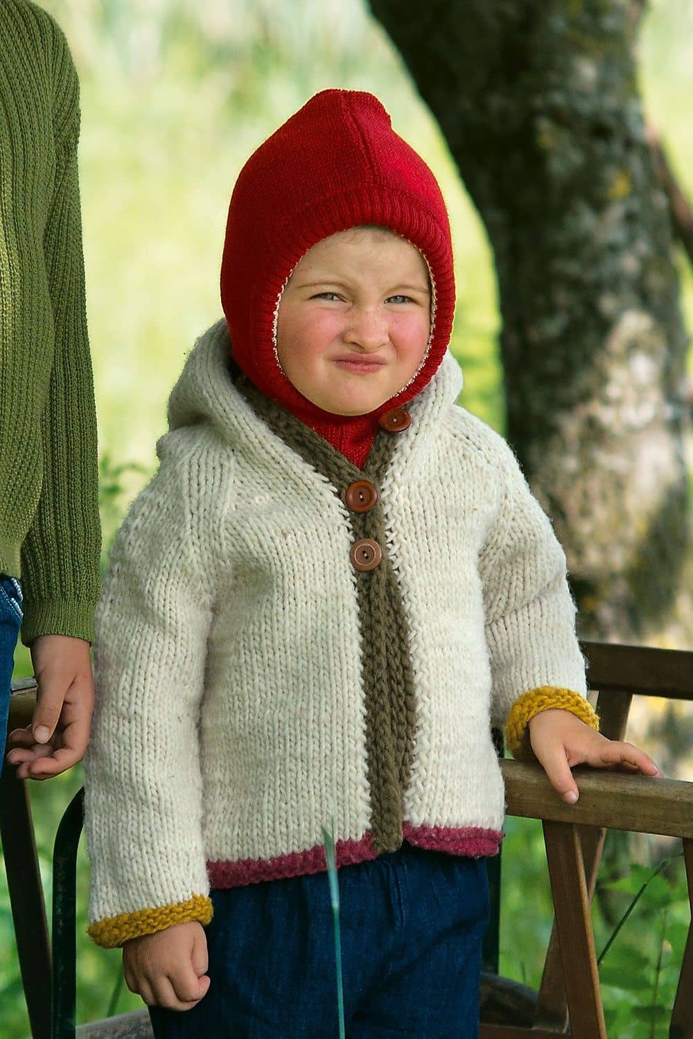 Kind mit weißer Weste trägt rote Schlupfmütze aus bio Wolle (kbT) und bio Baumwolle (kbA) vom Finkhof