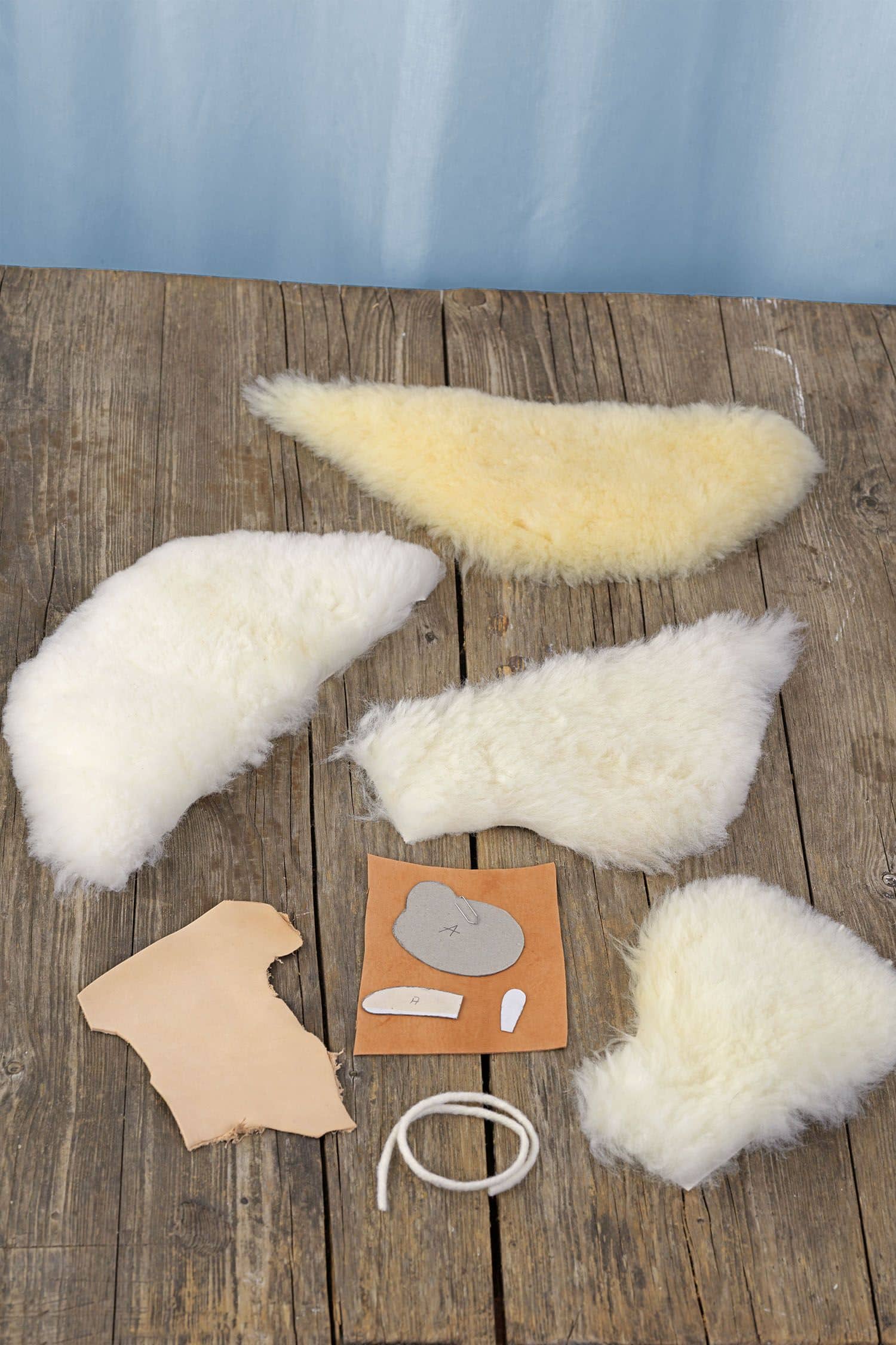 Einzelteile der Bastelpackung für ein Schäfchen Mobile vom Finkhof liegen auf einem braunen Holzboden