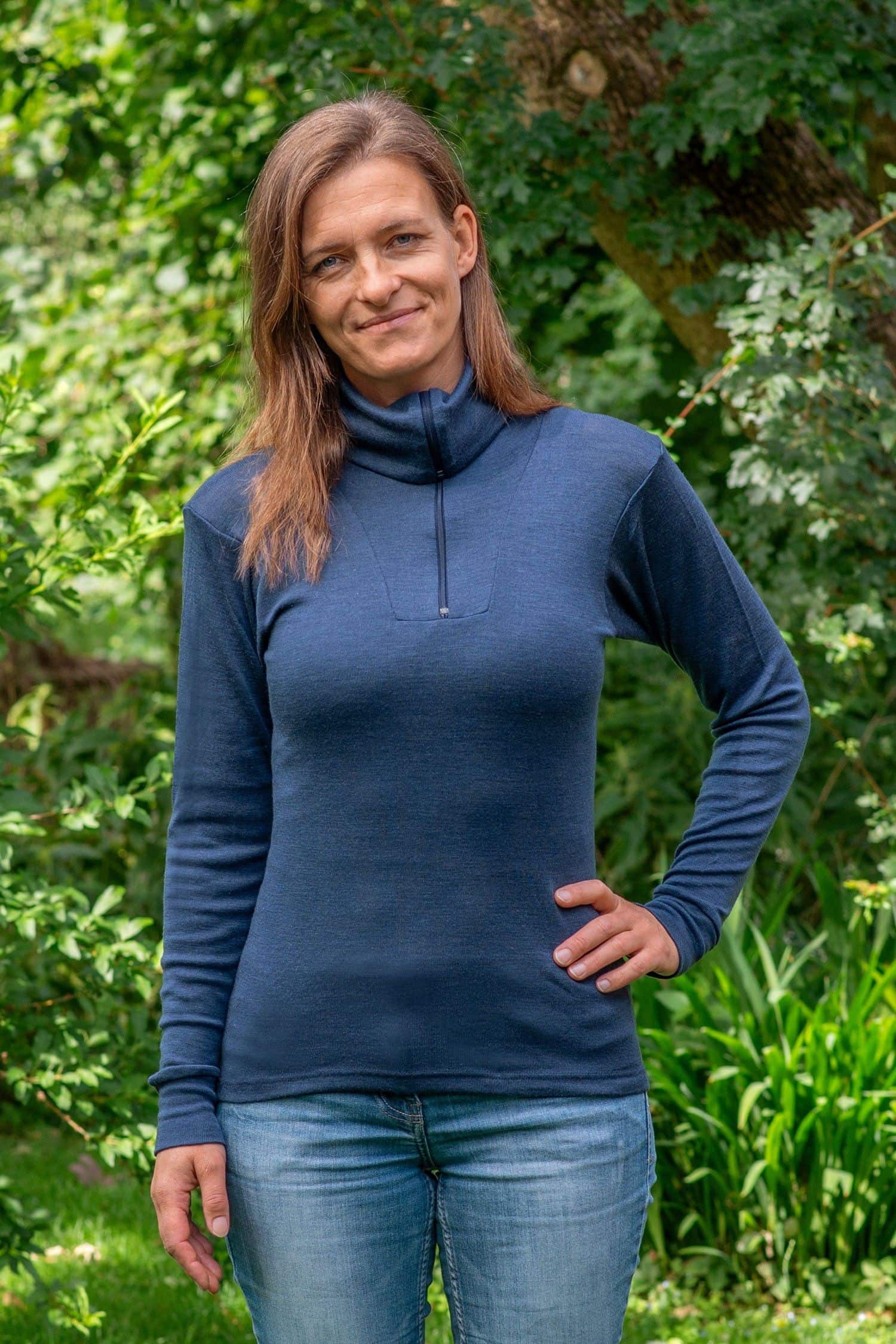 Frau steht im Garten und trägt Jeans und marineblauen Sportrolli aus bio Wolle (kbT) und Seide mit Reißverschluss