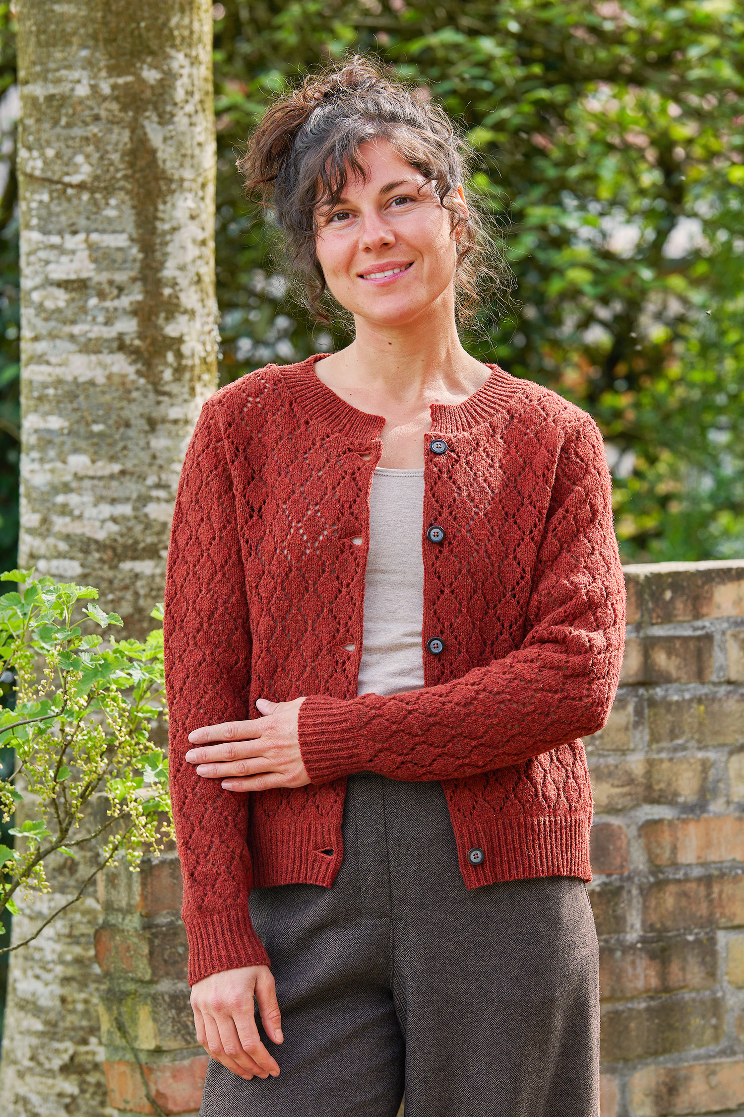 Frau trägt eine weite blaue Hose und eine rot orange Strickjacke mit Ajourmuster aus Bio-Wolle vom Finkhof