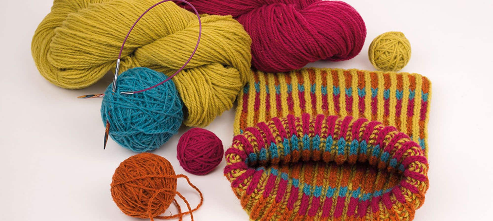 Strickanleitung Kinderloop Banner für bunt gemusterten Kinderloop und bunten Wollknäulen auf weißem Untergrund