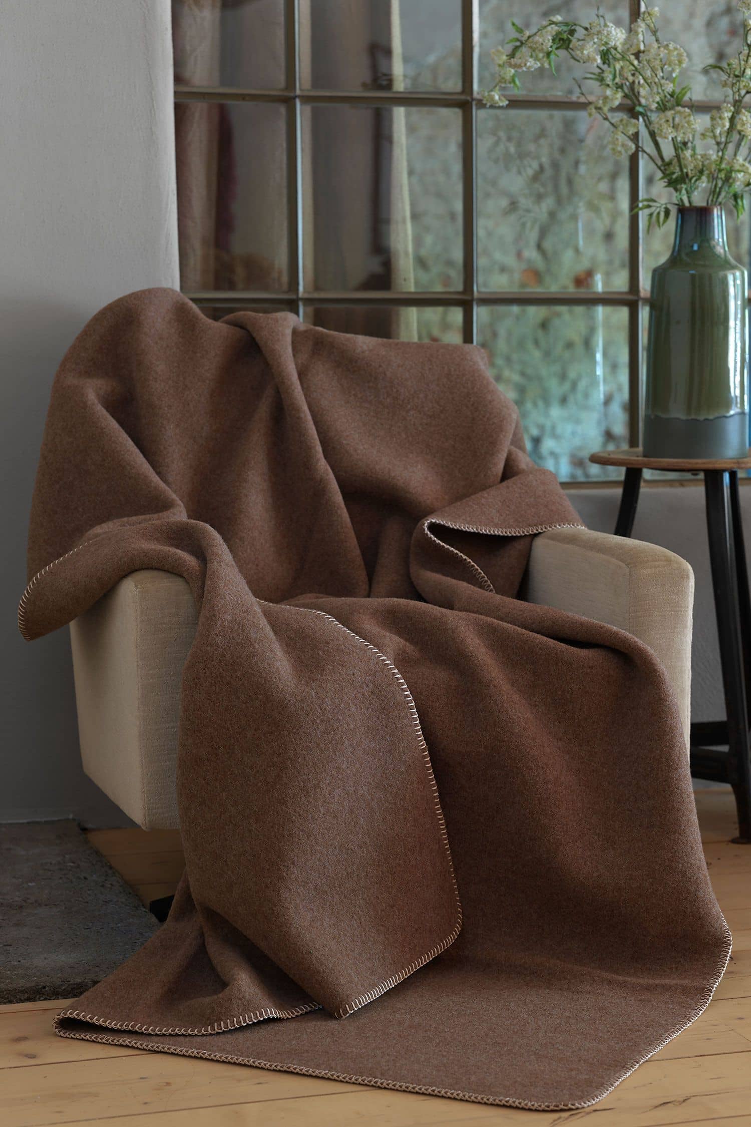 braune Wolldecke aus bioWolle (kbT) vom Juraschaf liegt auf beigem Sessel