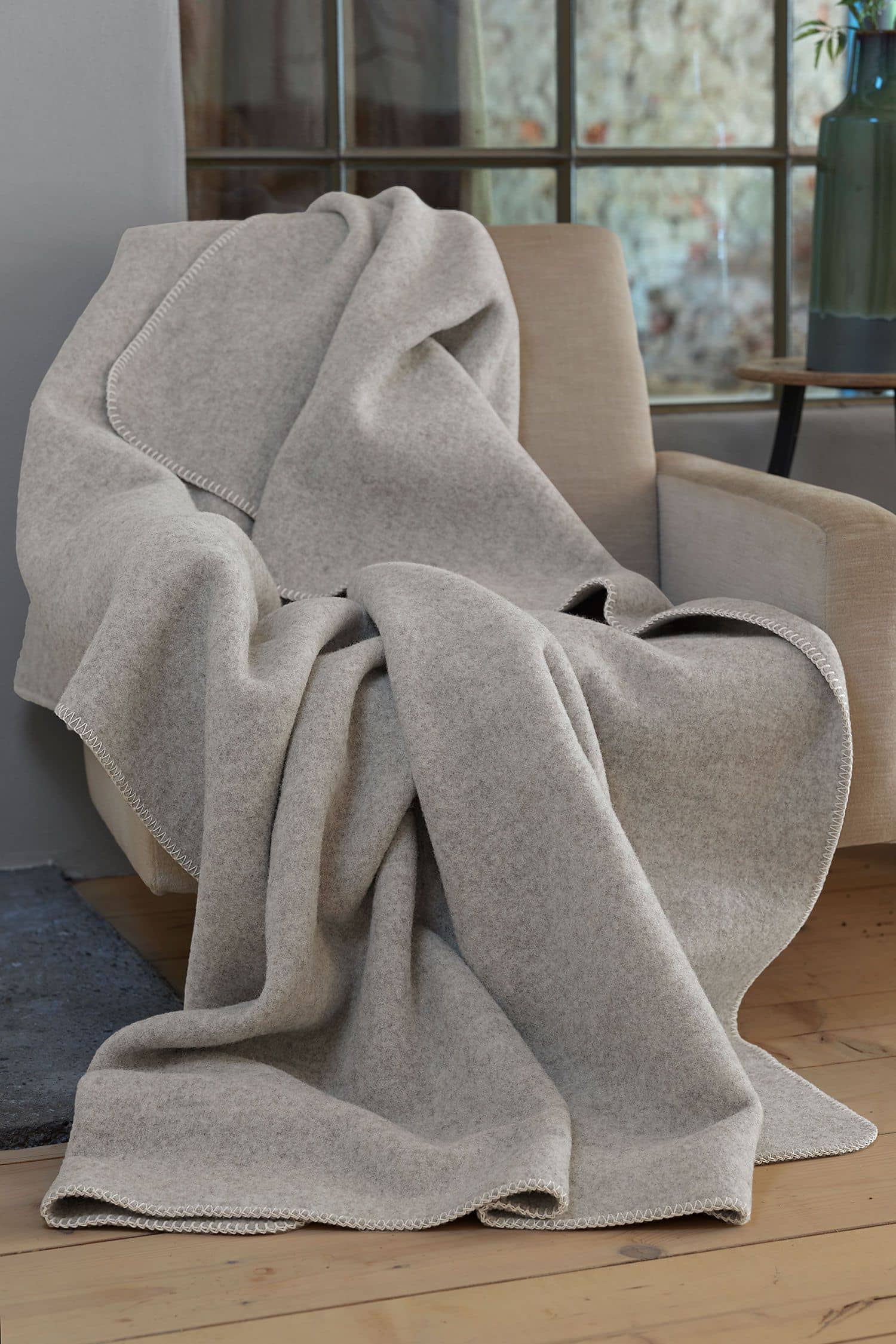 Merinolandschafdecke hellgrau 150 x 220 cm aus reiner Bio-Schurwolle hellgraue Wolldecke aus bio Merinowolle (kbT) vom Finkhof liegt auf beigem Sessel