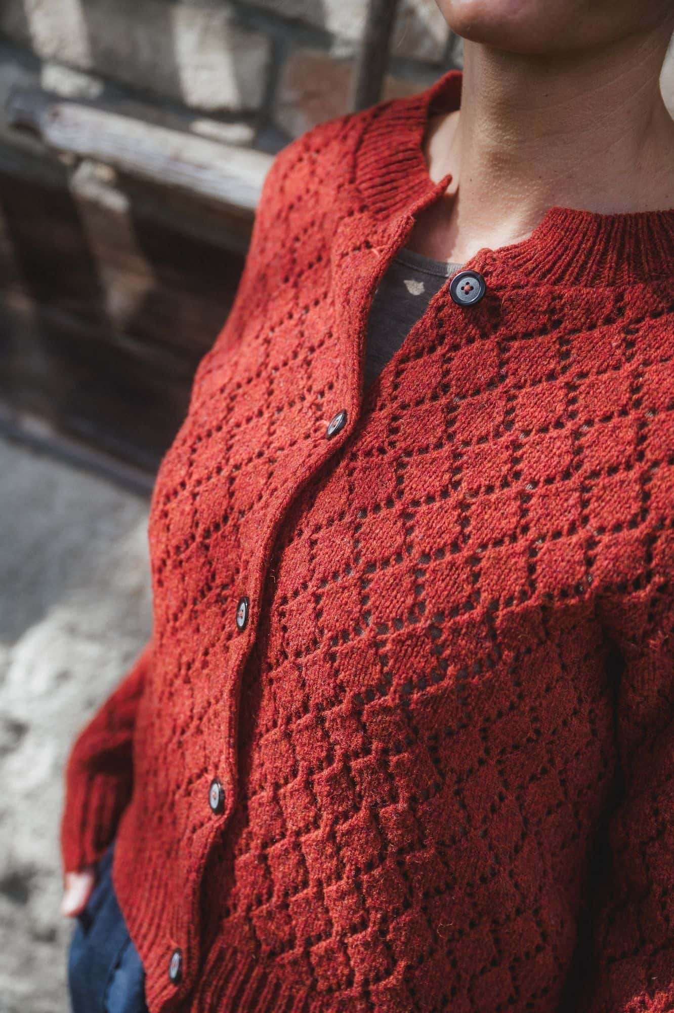 Nahaufnahme der Knopfleiste der rot orangen Strickjacke mit Ajourmuster aus Bio-Wolle vom Finkhof
