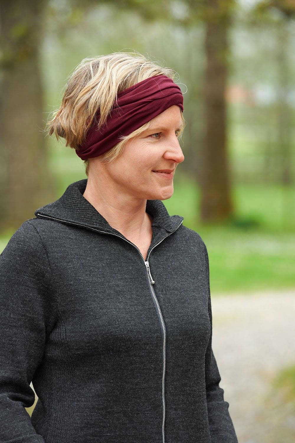 Frau mit grauer Weste trägt einen bordeauxroten Sportschal aus bio Wolle (kbT) und Seide als Stirnband