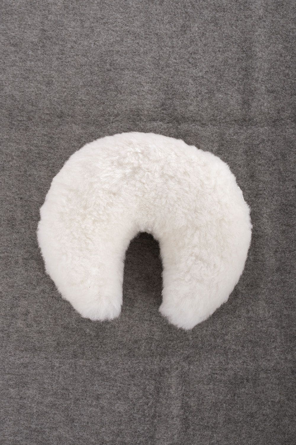 weißes Finkhof Fellhörnchen aus Schaffell und bio Rohwolle (kbT) liegt auf grauem Untergrund