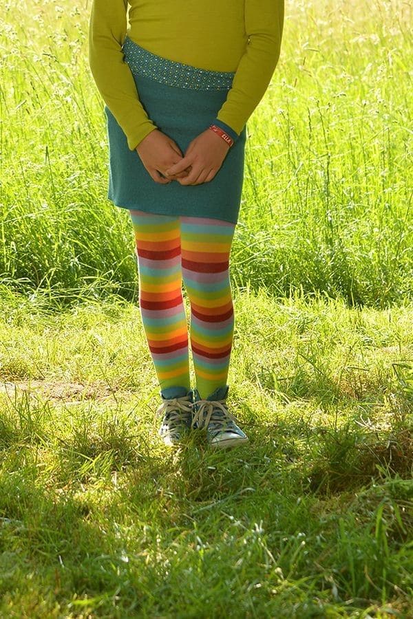 Kind trägt türkisen Rock, grünes Shirt und bunte gestreifte Leggings aus bio Baumwolle (kbA) und Elasthan