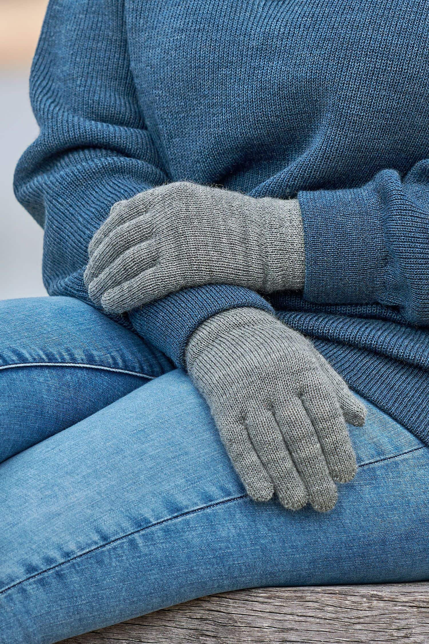 Nahaufnahme von Frau mit Troyer, Jeans und grauen Finkhof Strickhandschuhen mit Fingern aus bio Wolle (kbt)