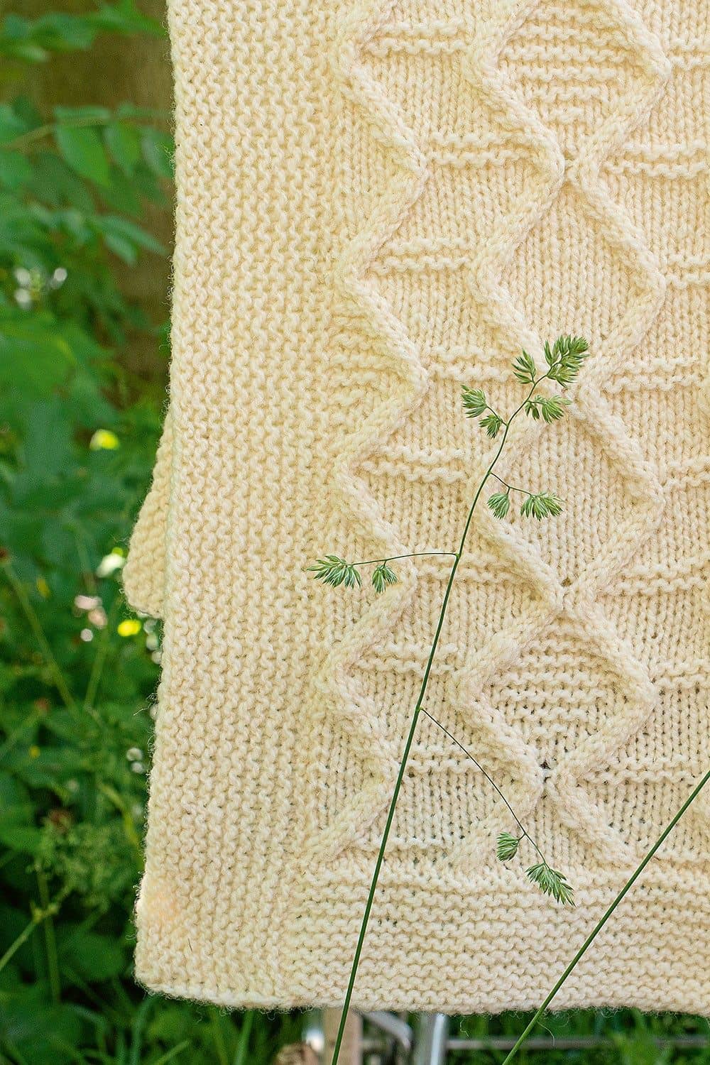Nahaufnahme einer naturweißen Strickdecke mit Zopfmuster als Beispiel für das Buch ,,Die schönsten Zopfmuster"