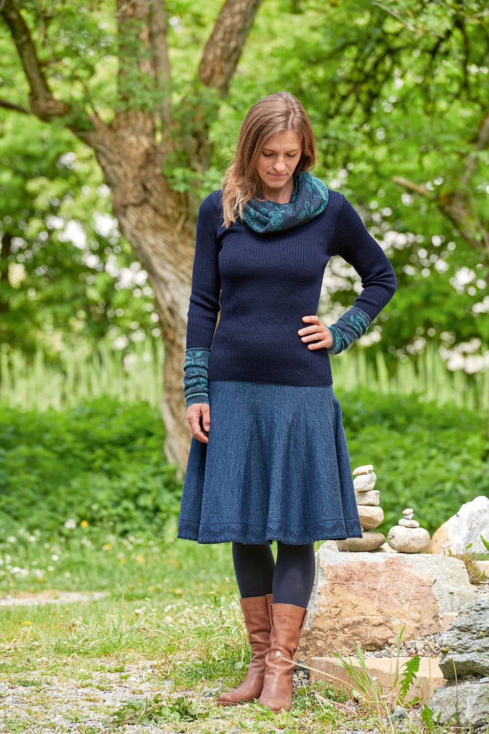Glockenrock Frau steht in Garten und trägt Finkhof Glockenrock aus bio Wolle (kbT), Rippshirt, Schal, Armstulpen und braunen Stiefeln