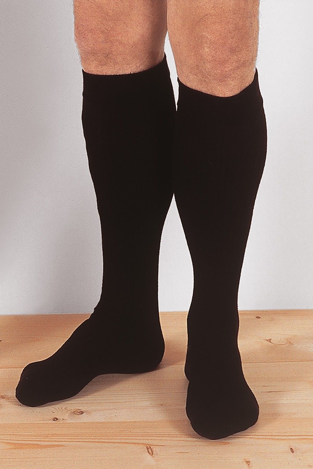 Person steht auf Holzboden und trägt schwarze warme Kniestrümpfe aus bio Wolle (kbT), Baumwolle (kbA), Elasthan vom Finkhof