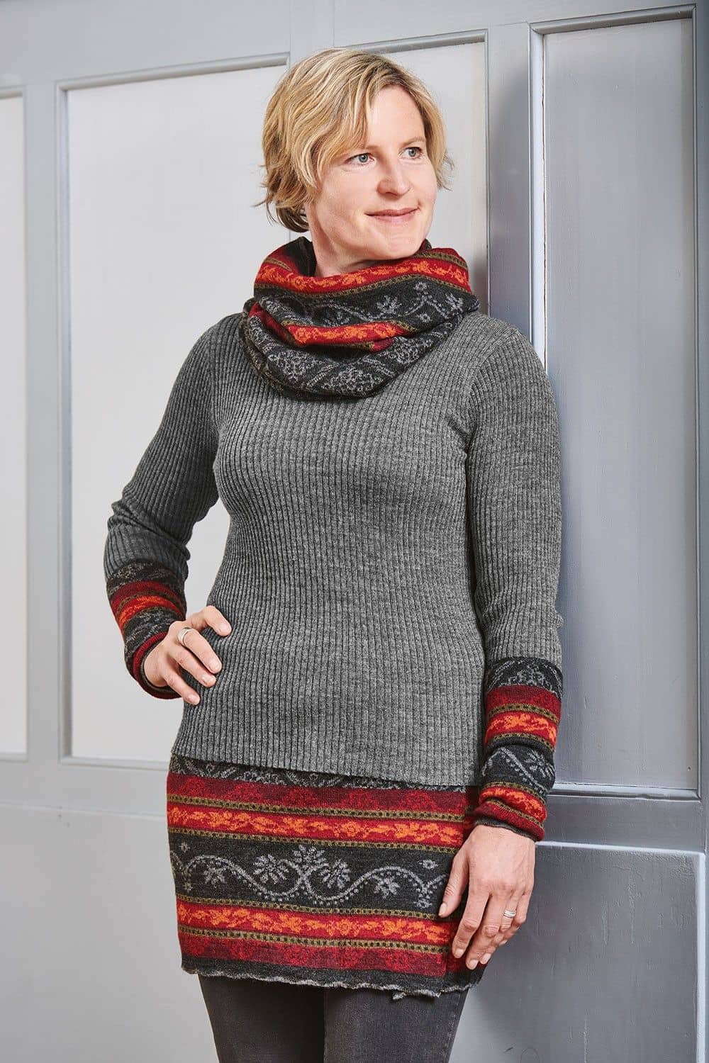 Frau trägt graues Rippshirt und rot grau gemusterten Cacheur, Armstulpen und Loopschal aus bio Wolle (kbT)