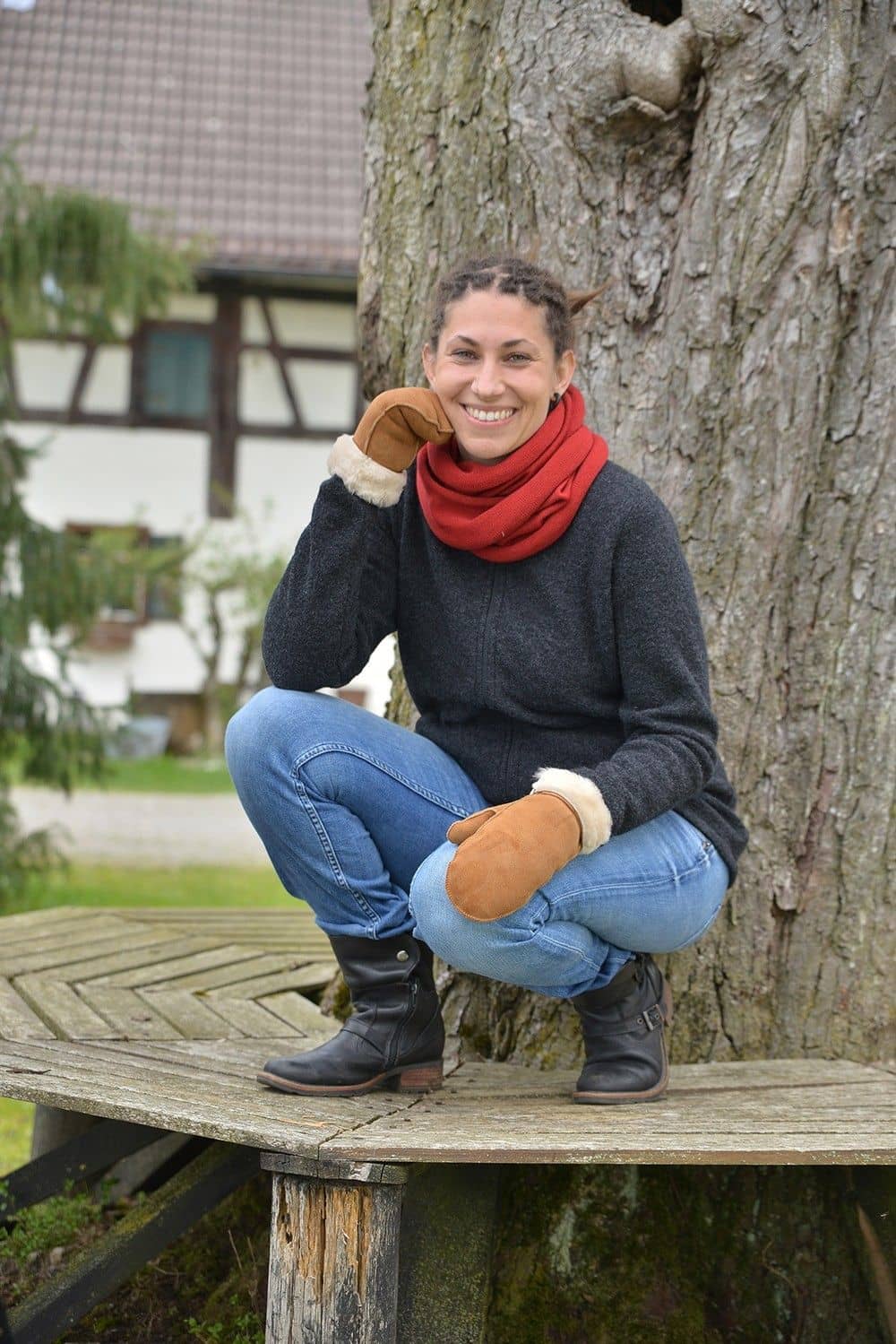 Frau kniet auf Bank und trägt hellbraune Fell- Fausthandschuhe aus Pelzvelour ohne Bund,graue Weste und roter Schal