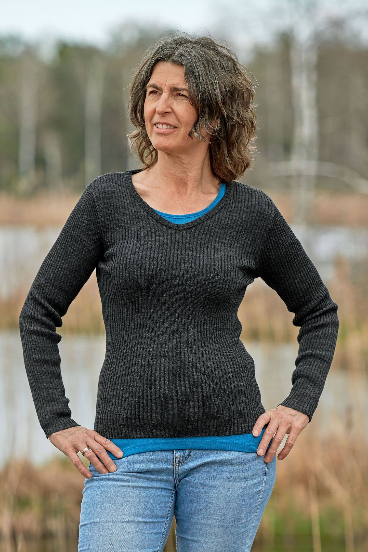 Frau mit Jeans und türkisem Shirt trägt dunkelgrauer Pulli mit Rippstoff und V Ausschnitt aus bio Finkhof Wolle (kbT)