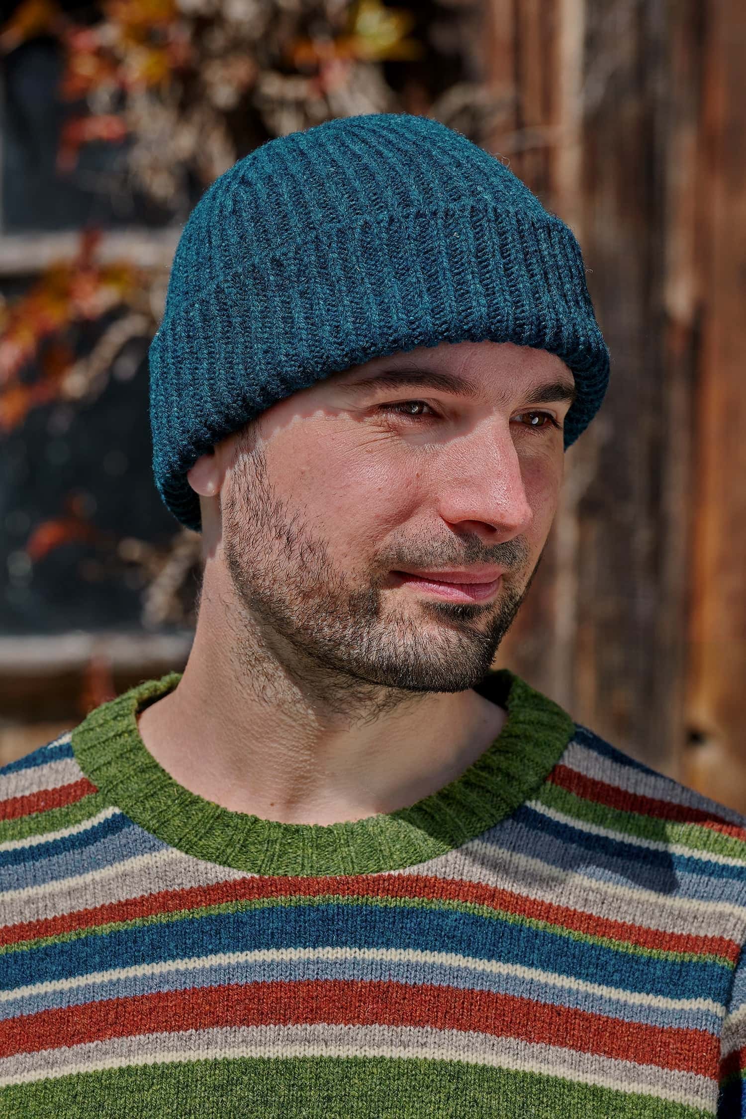 Mann trägt einen bunt gestreiften Strickpullover und eine seeblaue Fischermütze aus Bio-Wolle vom Finkhof