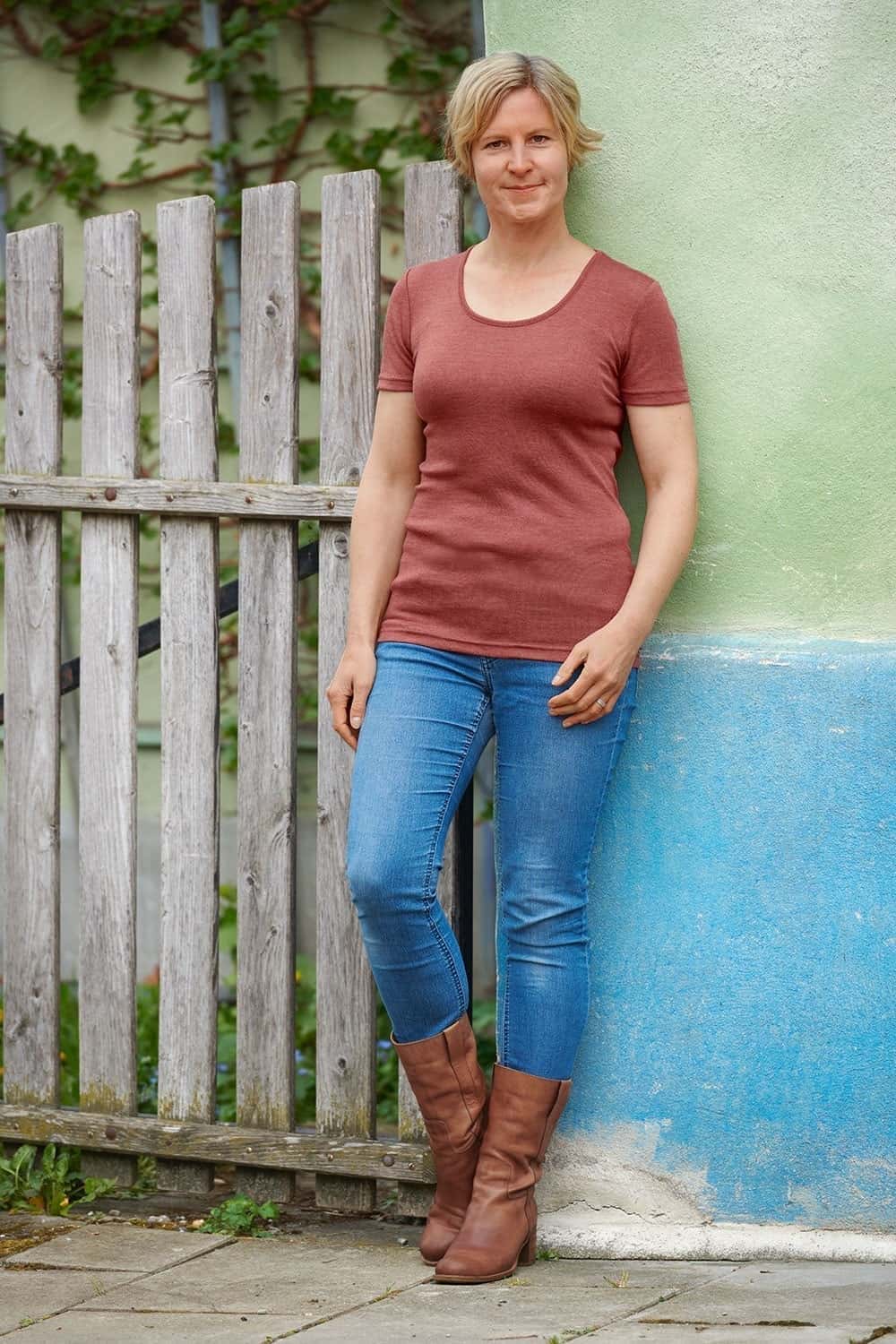 Frau lehnt mit Jeans und rostrotem Kurzarmshirt aus bio Wolle (kbT) und Seide an einer Wand