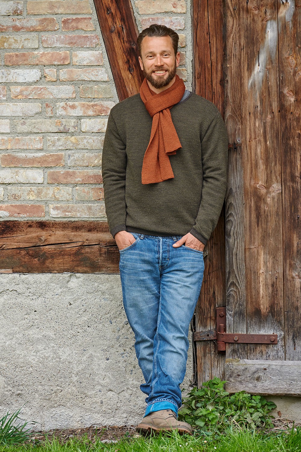 Mann mit grünem Pulli trägt orangen Strickschal aus bio Wolle (kbT) vom Finkhof
