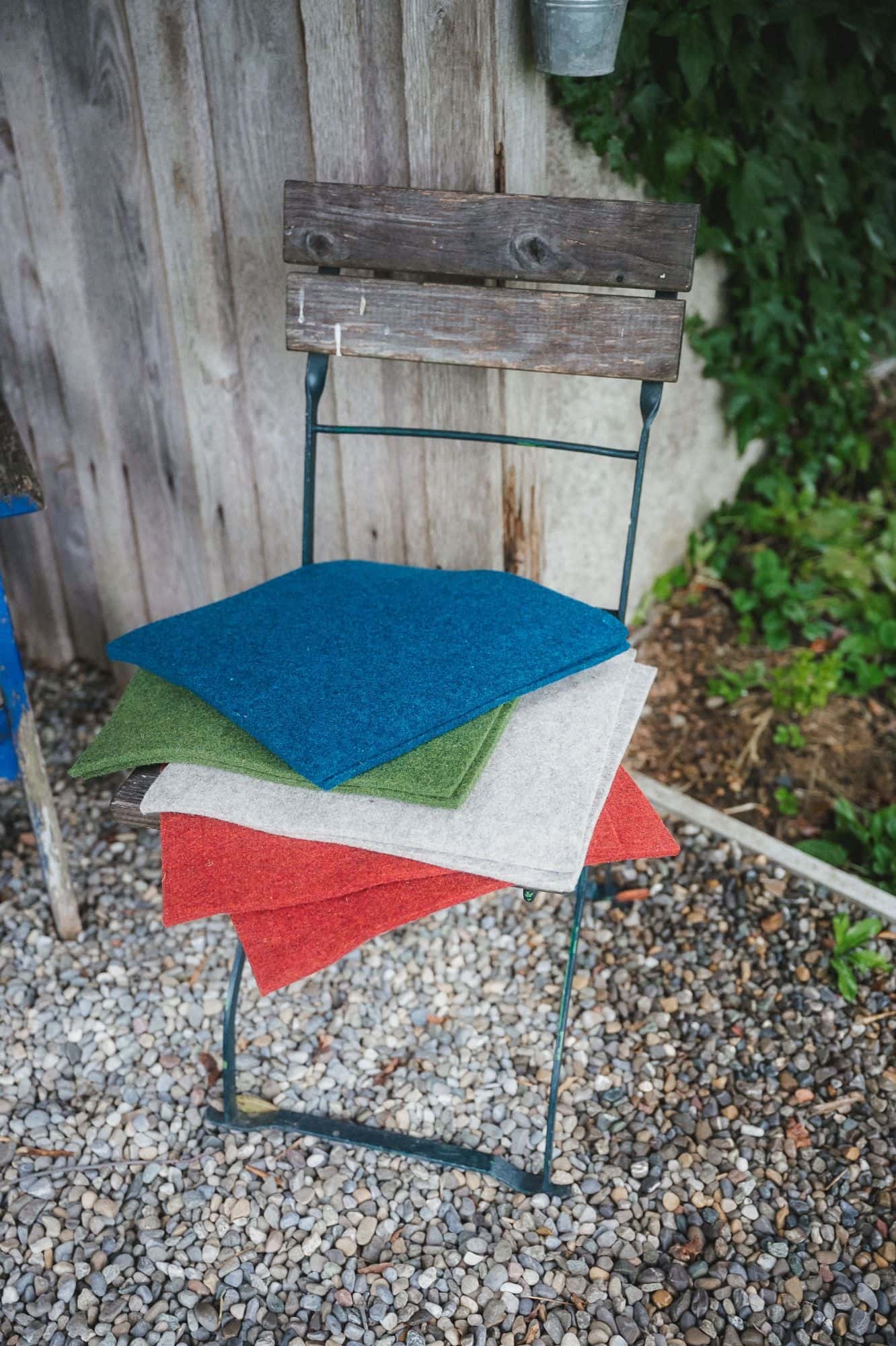 Finkhof-Sitzauflagen aus Nadelfilz quadratisch Finkhof Nadelfilz in verschiedenen Farben aus bio Wolle (kbT) auf Gartenstuhl vor einer Holzwand