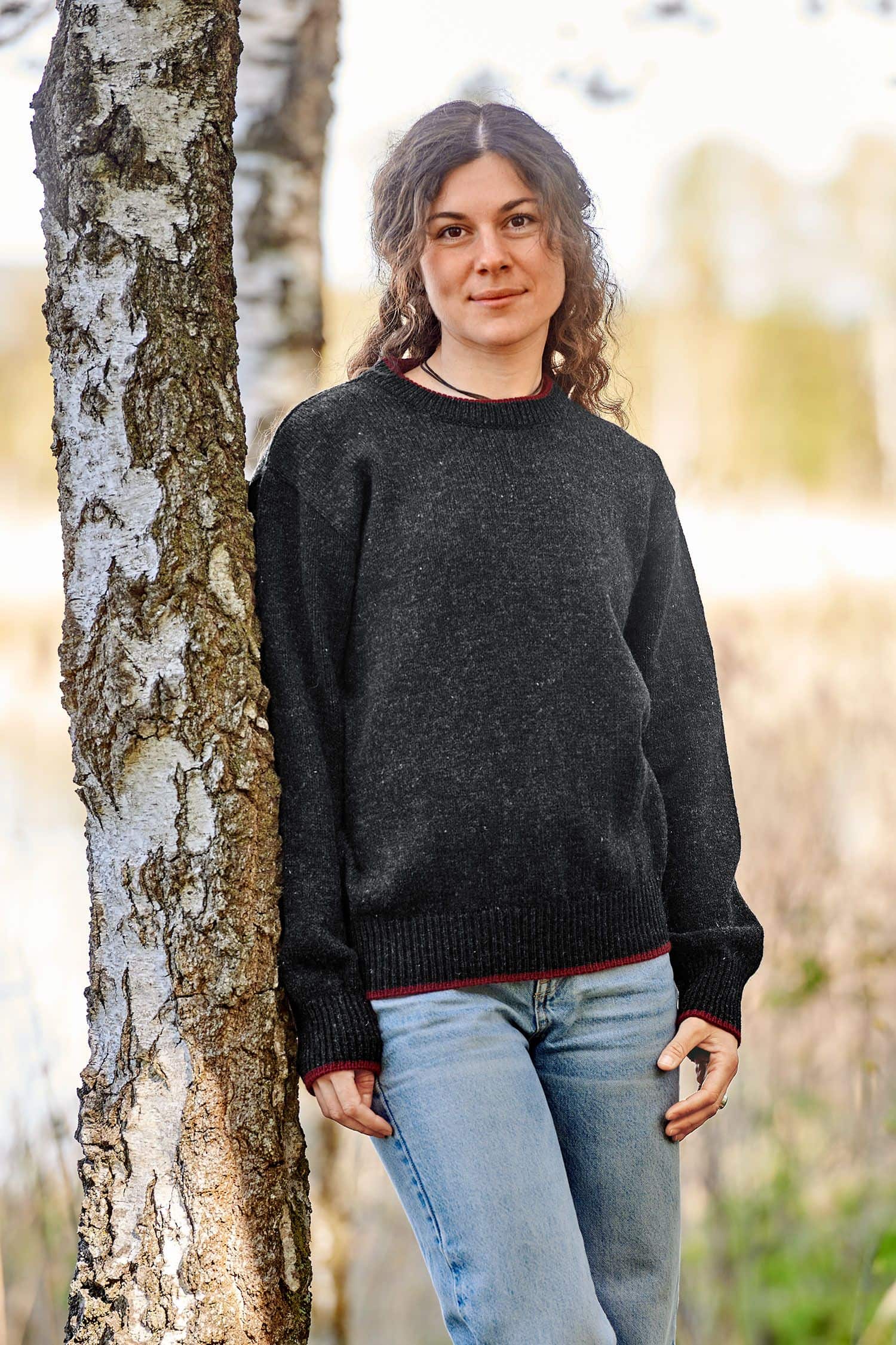Frau lehnt an Baum und trägt einen anthrazitgrauen Finkhof Pullover aus bio Wolle (kbT)