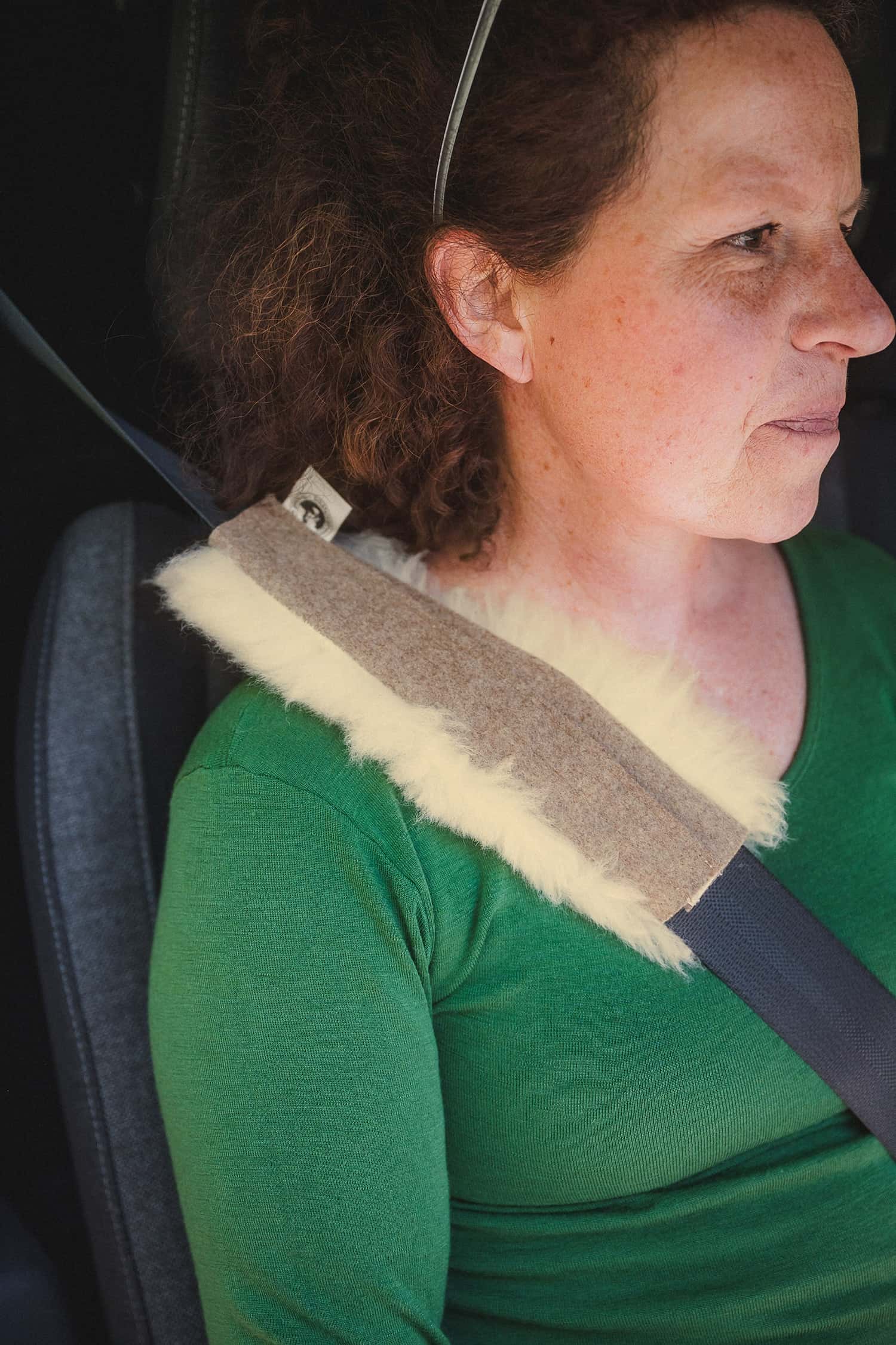 Frau mit grünem Shirt sitzt im Auto und hat am Gurt ein Polster aus relugan gegerbtem Schaffell und Bio-Loden vom Finkhof
