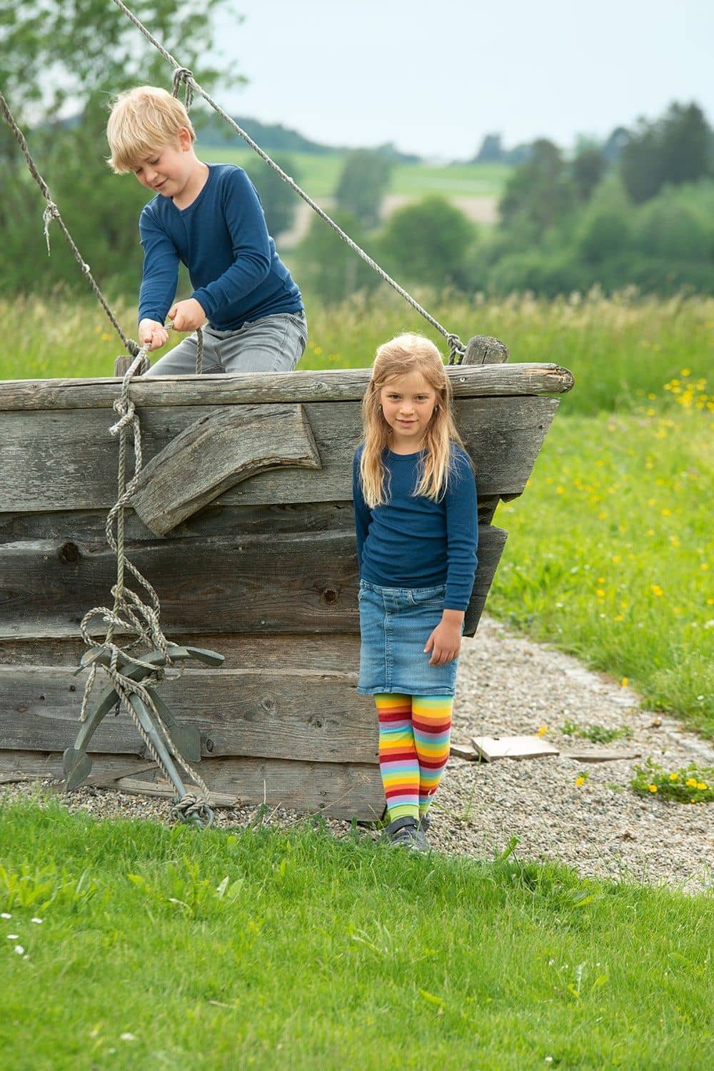 Kinder spielen auf Holzschiff und tragen dunkelblaue Langarmshirts aus bio Wolle (kbT) und Seide mit Jeans und Rock