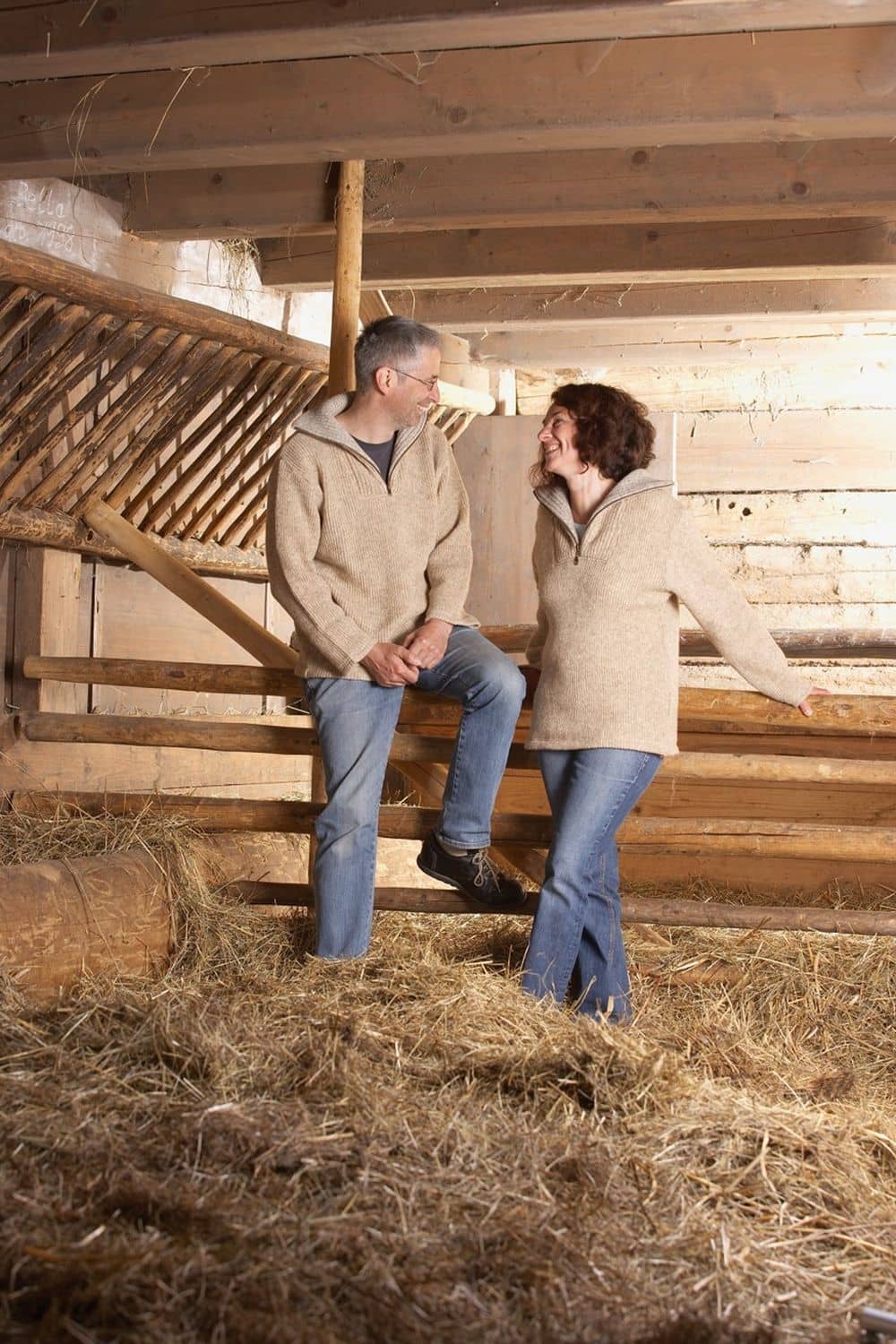 Mann und Frau im Stall tragen graue Finkhof Troyer aus bio Merinowolle (kbT)