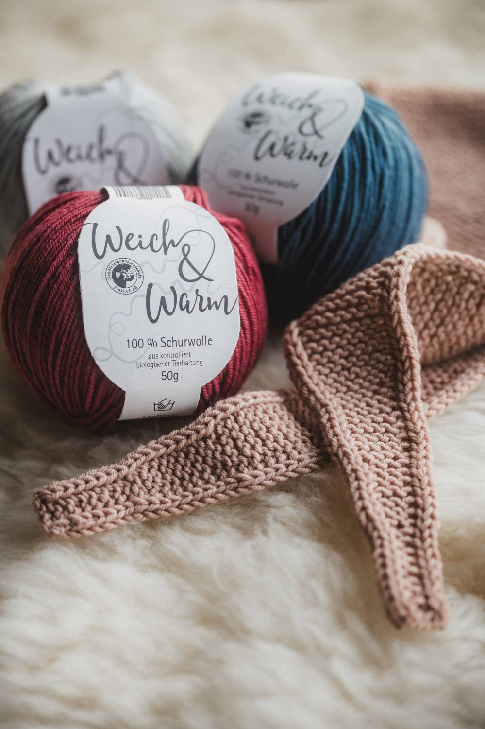 Detailaufnahme von rosafarbenem Mini-Schal mit der Finkhof Weich&Warm Wolle auf einem weißen Fell