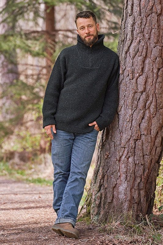 Mann mit Jeans an Baum gelehnt trägt anthraziten Finkhof Troyer mit Zipper aus bio Wolle (kbT)