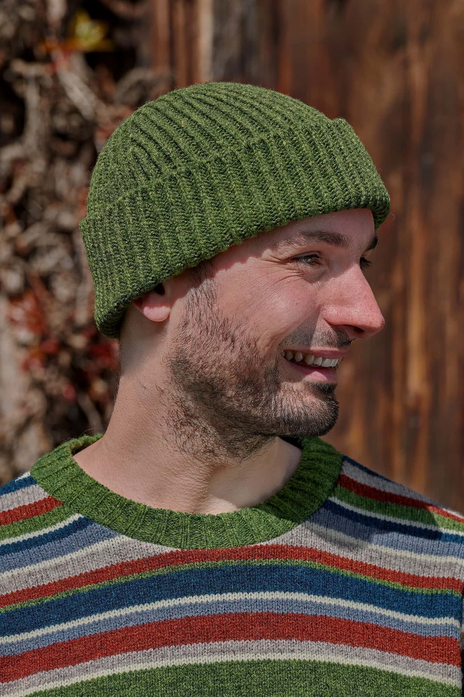 Mann trägt einen bunt gestreiften Pullover und eine grüne Fischermütze aus Bio-Wolle vom Finkhof