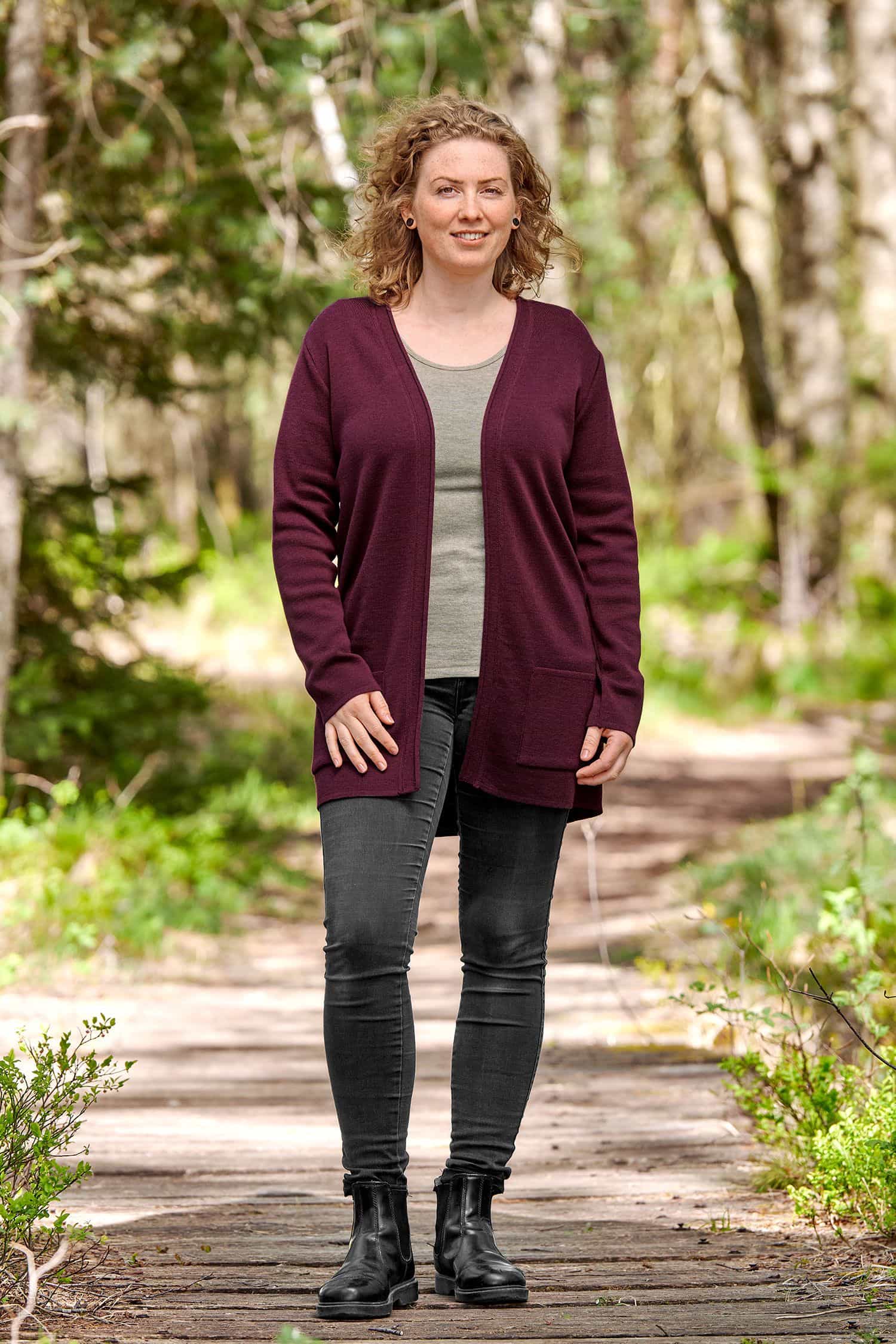 Frau mit schwarzer Jeans und einfarbigem Shirt trägt burgunderroten langen Cardigan aus bio Wolle (kbT)