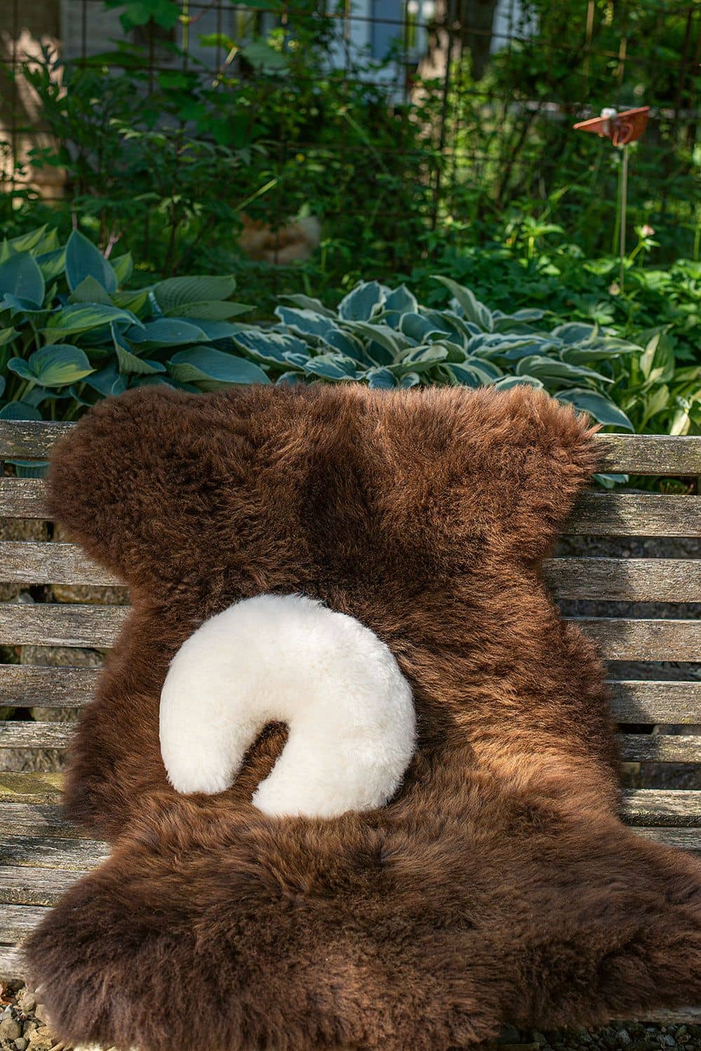 weißes Finkhof Fellhörnchen aus Schaffell und bio Rohwolle (kbT) liegt mit braunem Schaffell auf einer Bank