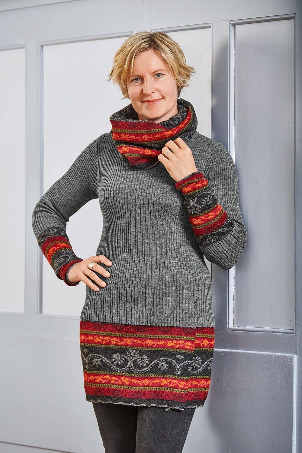 Frau trägt graues Rippshirt und rot grau gemusterten Cacheur, Armstulpen und Loopschal aus bio Wolle (kbT)