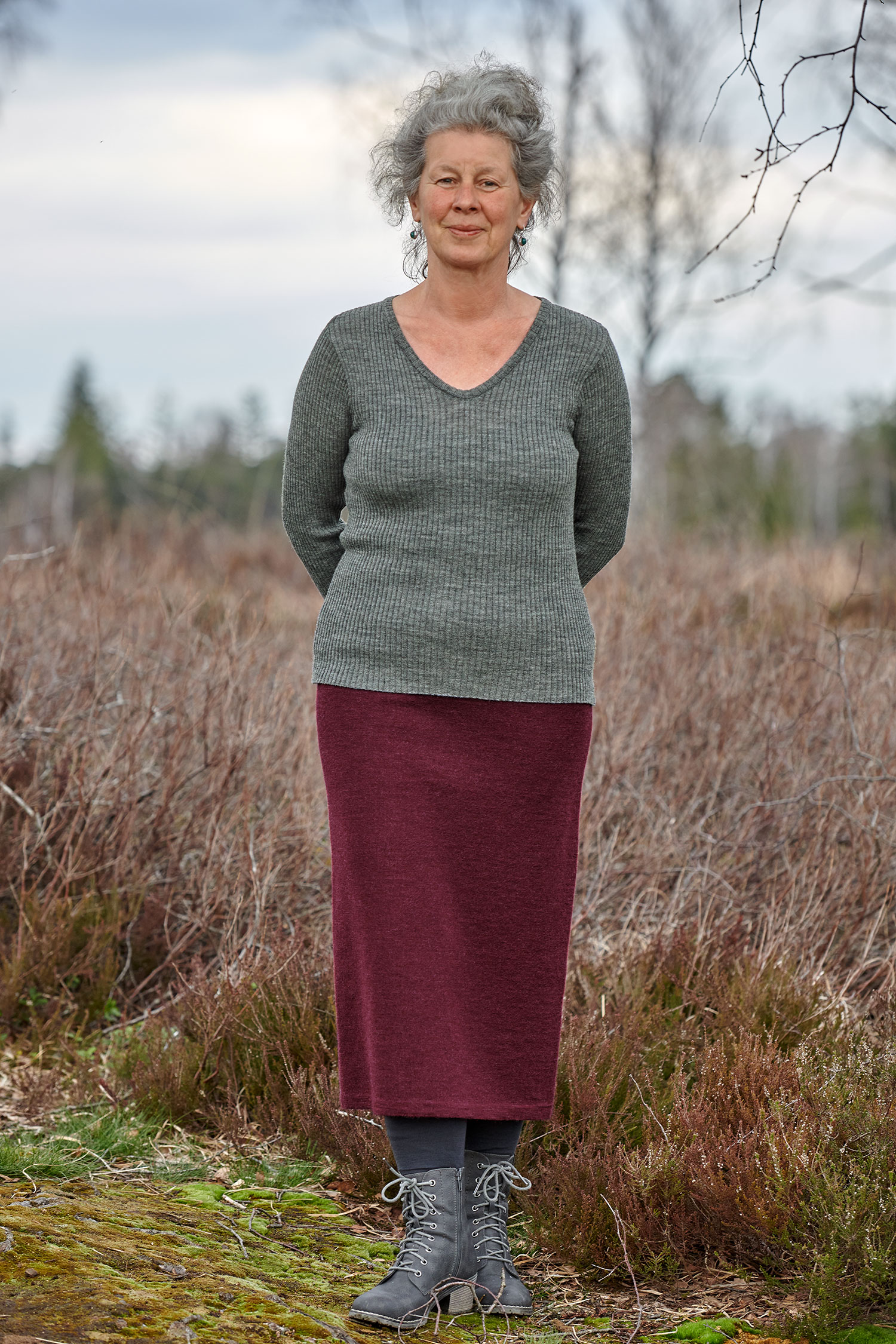 Frau trägt burgunderrotes Strickkleid aus bio Wolle (kbT) und darüber ein graues Rippshirt