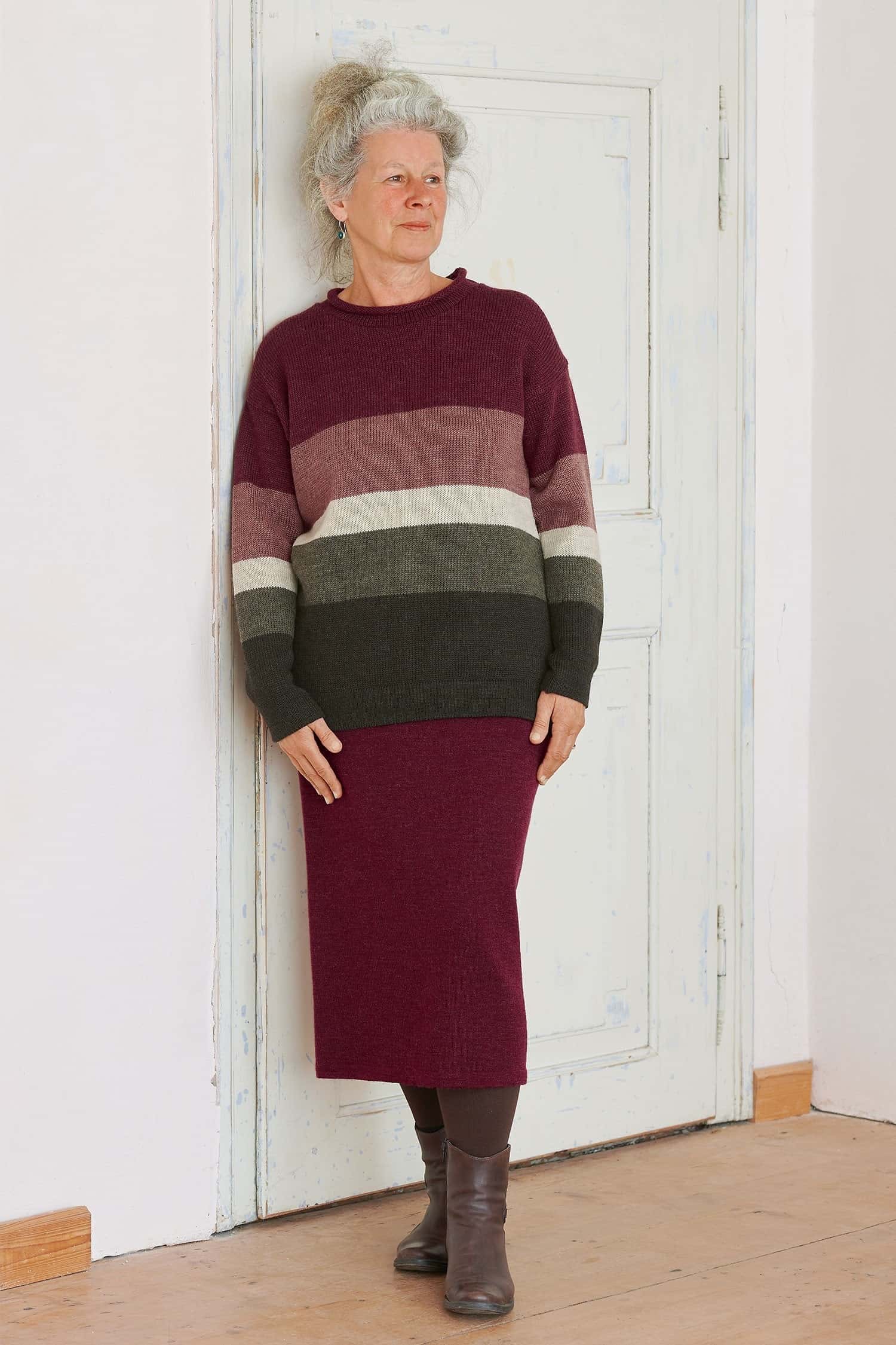 Frau mit weinrotem Rock und grün rotem Streifenpullover aus bio Wolle (kbT) lehnt an einer Tür