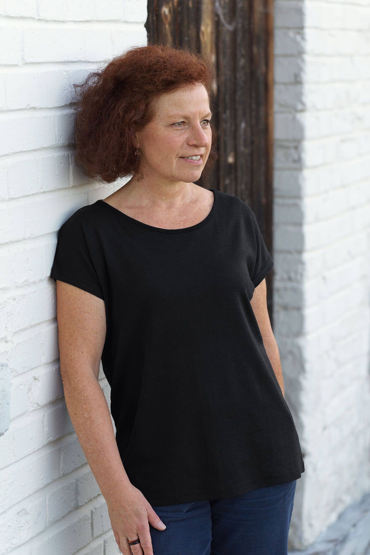 Frau trägt schwarzes oversize Shirt aus bio Wolle (kbT) und Seide und lehnt sich an Wand